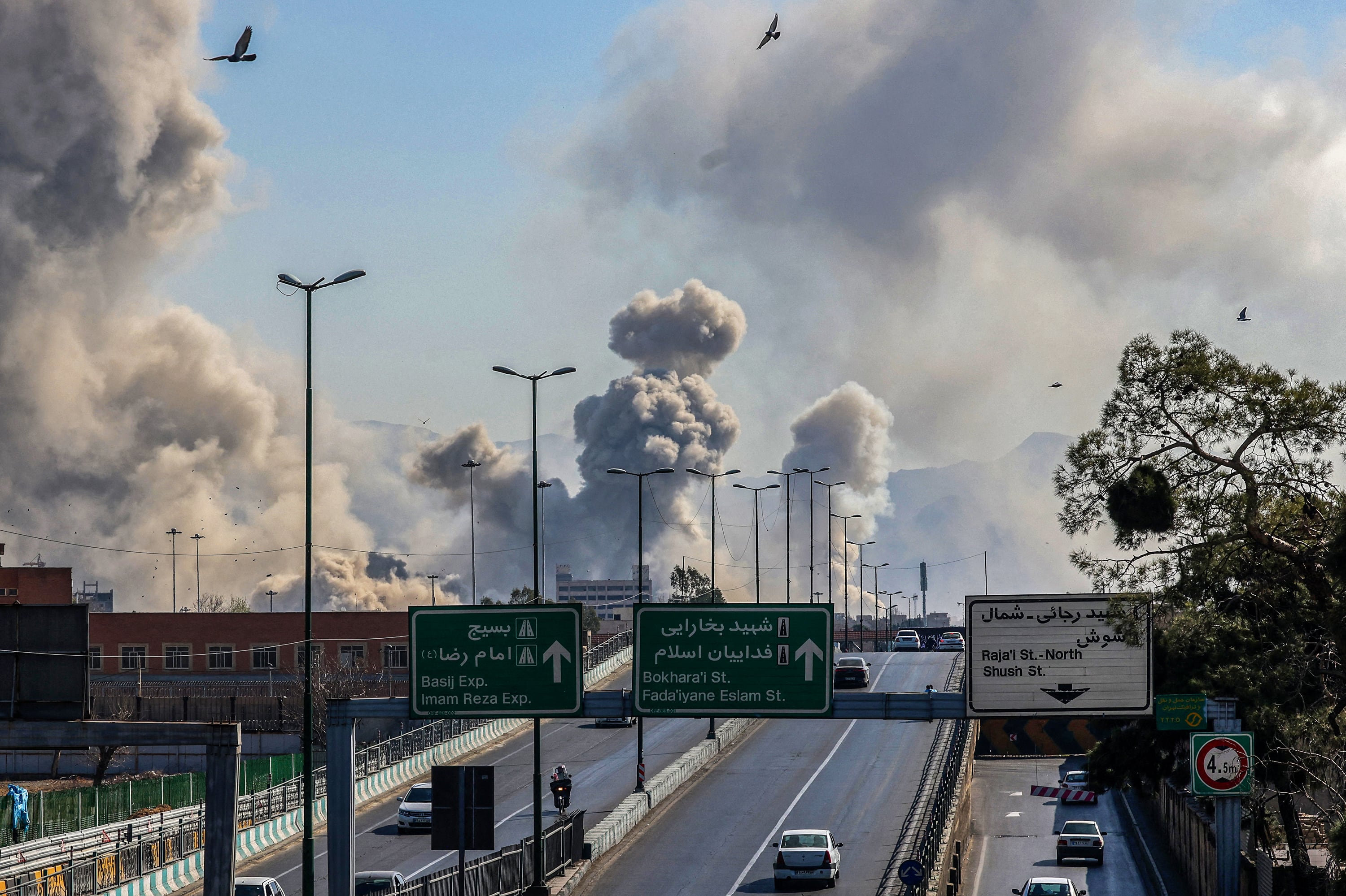Motorists drive along an expressway as plumes of smoke rise after a strike in Tehran on March 5, 2026. Israel pounded Tehran with fresh strikes and Iran targeted Kurdish guerilla groups in Iraq on March 5 as a spiralling war in the Middle East engulfed the entire region. (Photo by ATTA KENARE / AFP)