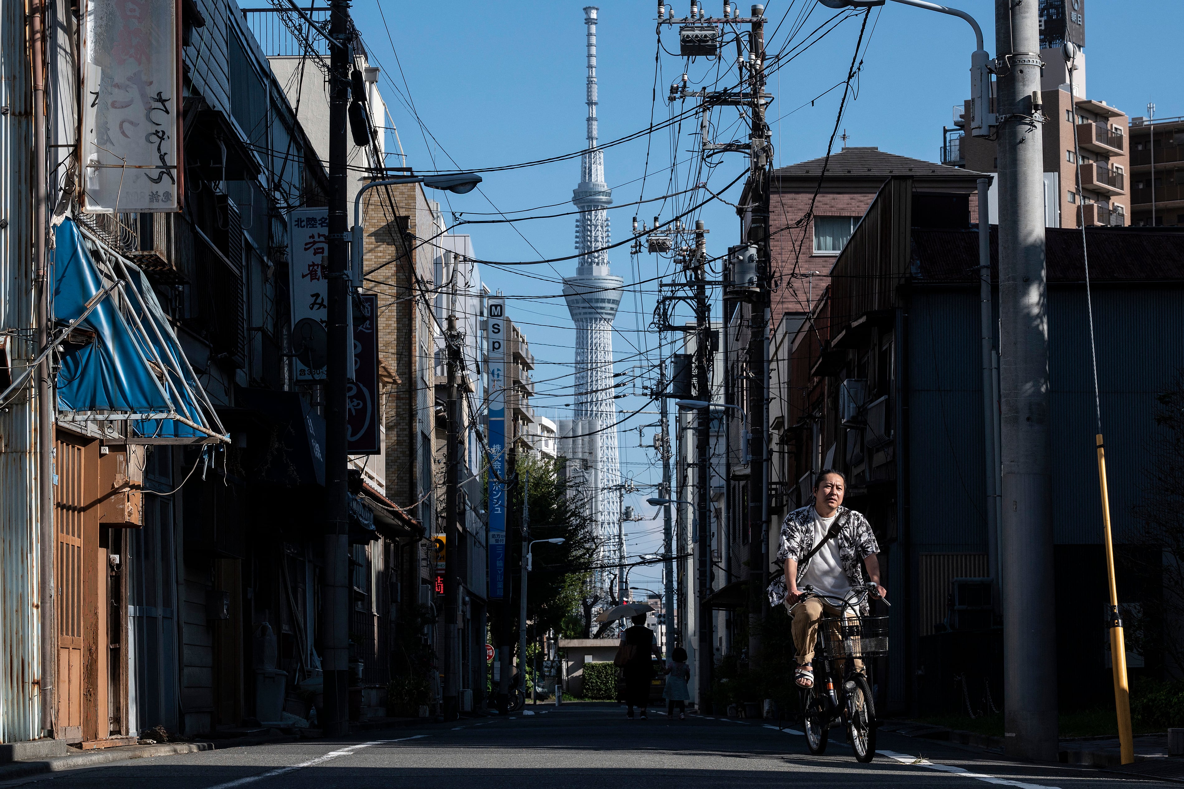 A man rides a bicycle past old buildings as the Tokyo Skytree, one of the world's tallest buildings at 634 metres (2,080 feet), is pictured behind, along a street in the Minowa area of Taito Ward in Tokyo