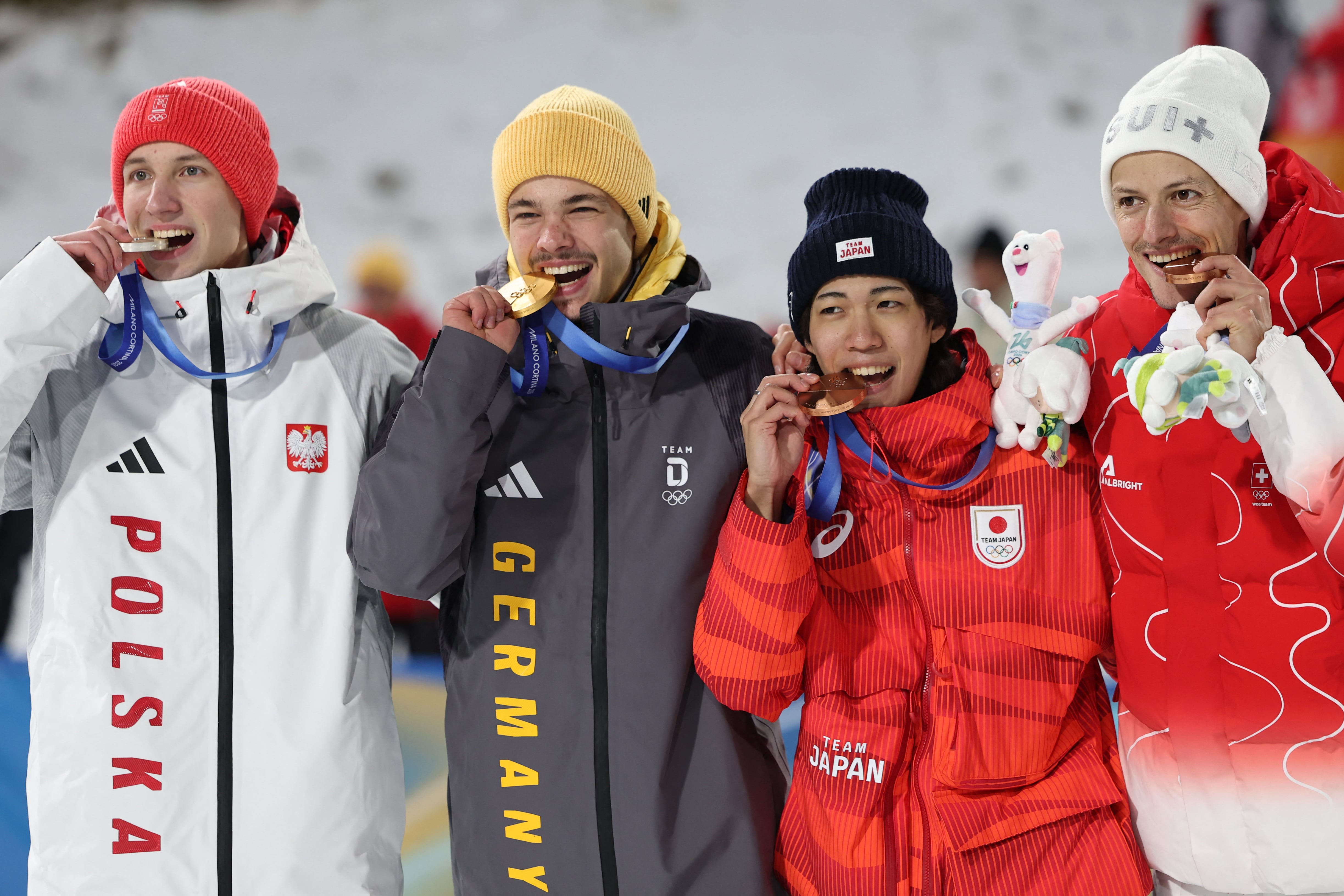 (From L) Silver medallist Poland's Kacper Tomasiak, gold medallist Germany's Philipp Raimund and Bronze medallists who tied for third place Japan's Ren Nikaido and Switzerland's Gregor Deschwanden bite their medal as they celebrate on the podium for the men's ski jumping normal hill individual final round of the Milano Cortina 2026 Winter Olympic Games at Predazzo Ski Jumping Stadium in Predazzo (Val di Fiemme), on February 9, 2026. (Photo by Anne-Christine POUJOULAT / AFP)