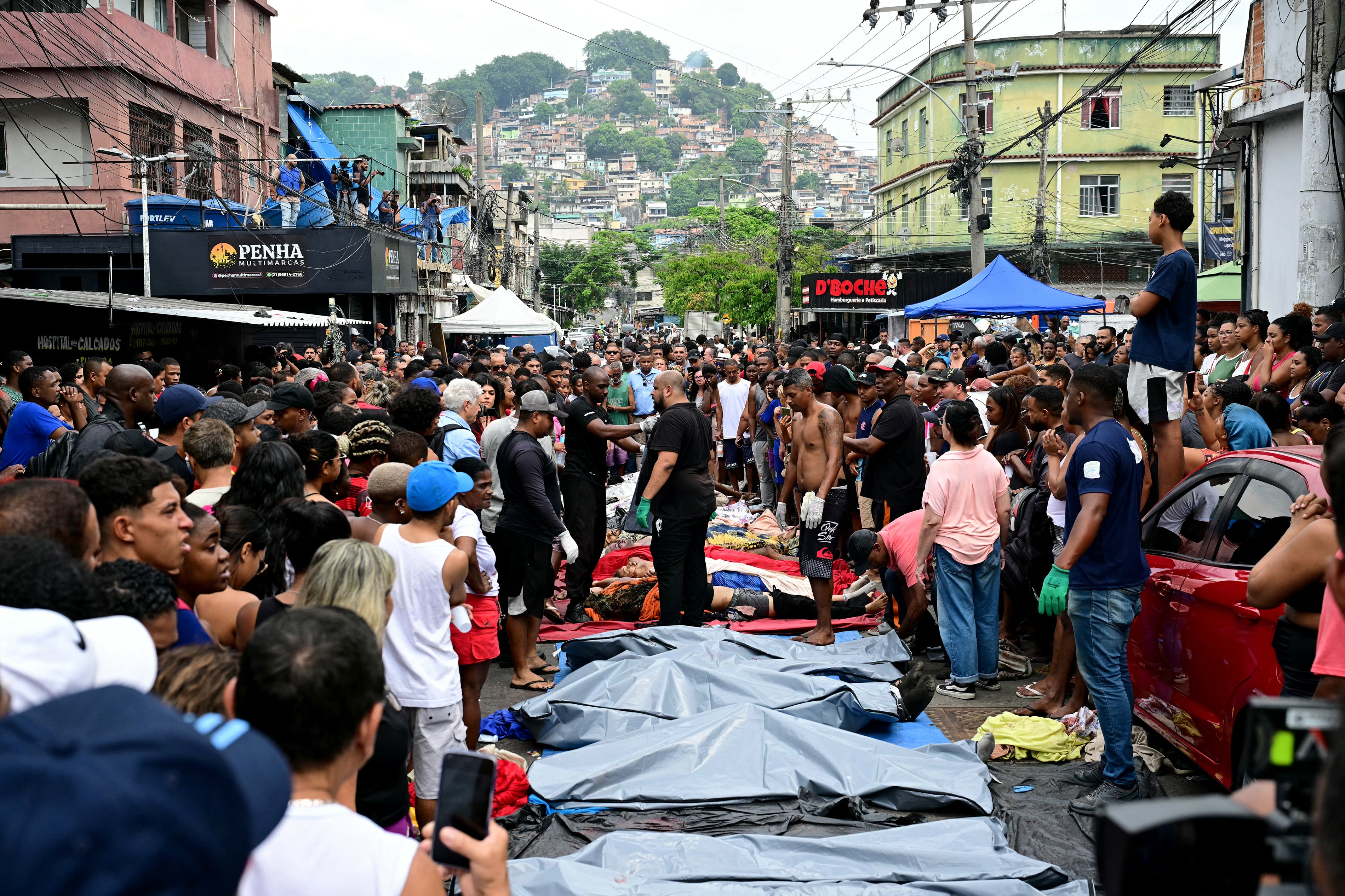 Residentes se encuentran junto a los cuerpos alineados en la plaza São Lucas de la favela Vila Cruzeiro, en el complejo Penha de Río de Janeiro, Brasil, el 29 de octubre de 2025, tras la Operación Contención. Residentes de una favela de Río de Janeiro alinearon más de 50 cuerpos en una plaza de su barrio de bajos ingresos el 29 de octubre, un día después de la operación policial más sangrienta en la historia de la ciudad, informó AFP. (Foto de Pablo PORCIUNCULA / AFP)