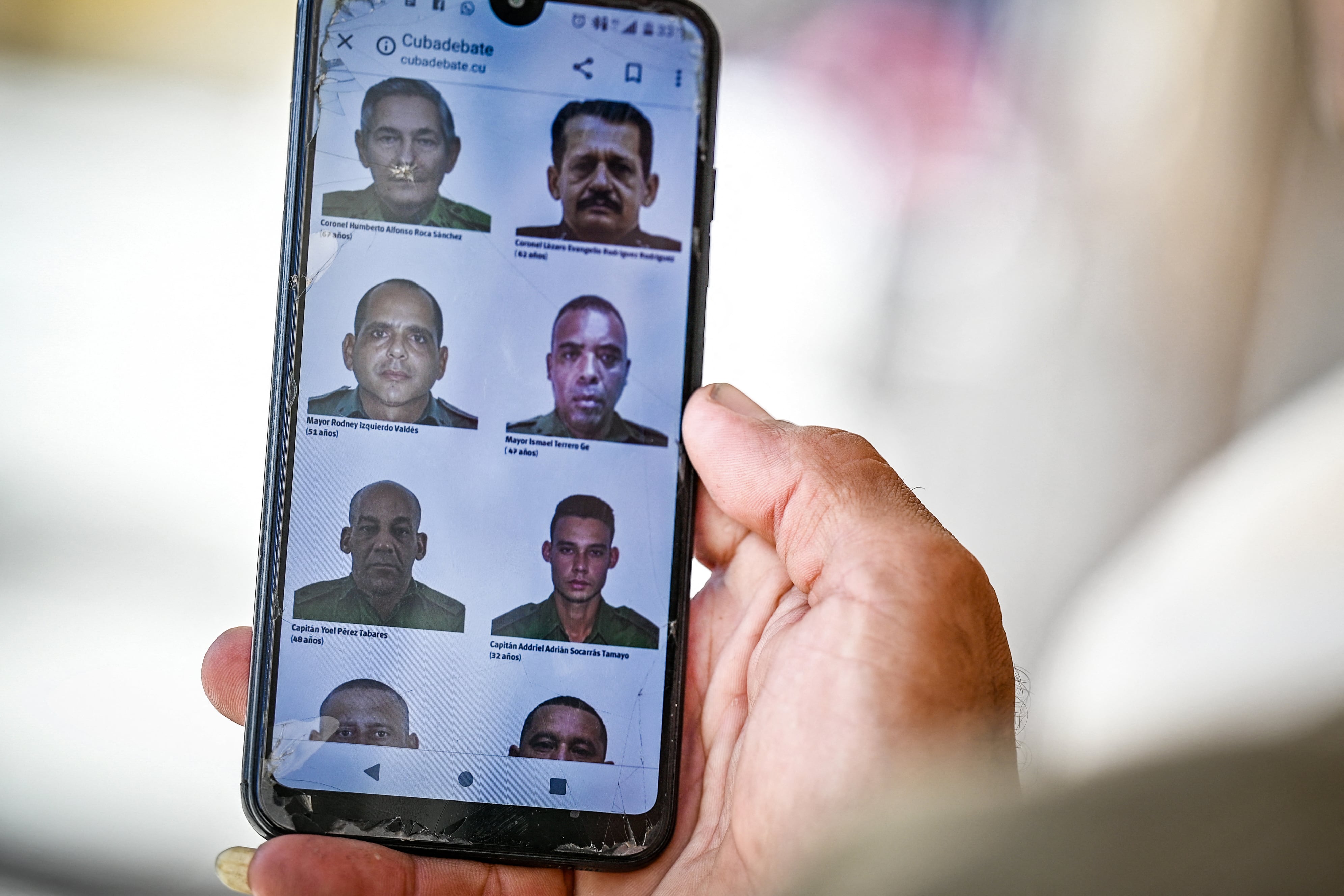 A man in Havana goes through the official website of the Cuban government cubadebate.cu on his mobile phone, where images of some of the 32 Cuban officers and soldiers killed during the US military intervention in Venezuela are displayed, on January 6, 2026. US forces killed 55 Venezuelan and Cuban military personnel during their stunning raid to capture Nicolas Maduro, tolls published by Caracas and Havana showed on January 6. Cuba, which had already announced that 32 members of its armed forces and interior ministry security personnel assigned to duties in Caracas were killed in the raids, also listed its dead. (Photo by Adalberto ROQUE / AFP)