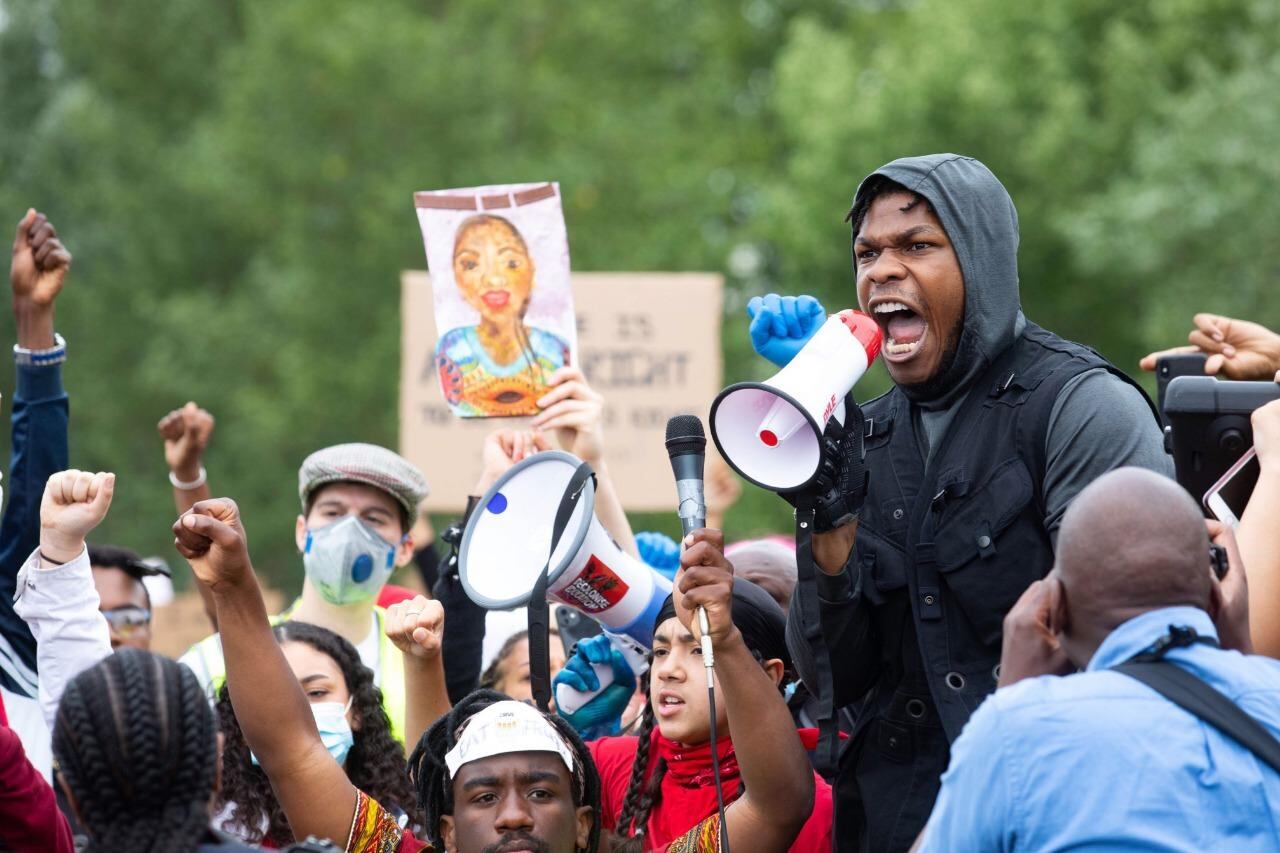  John Boyega arengando a la multitud megáfono en mano. 