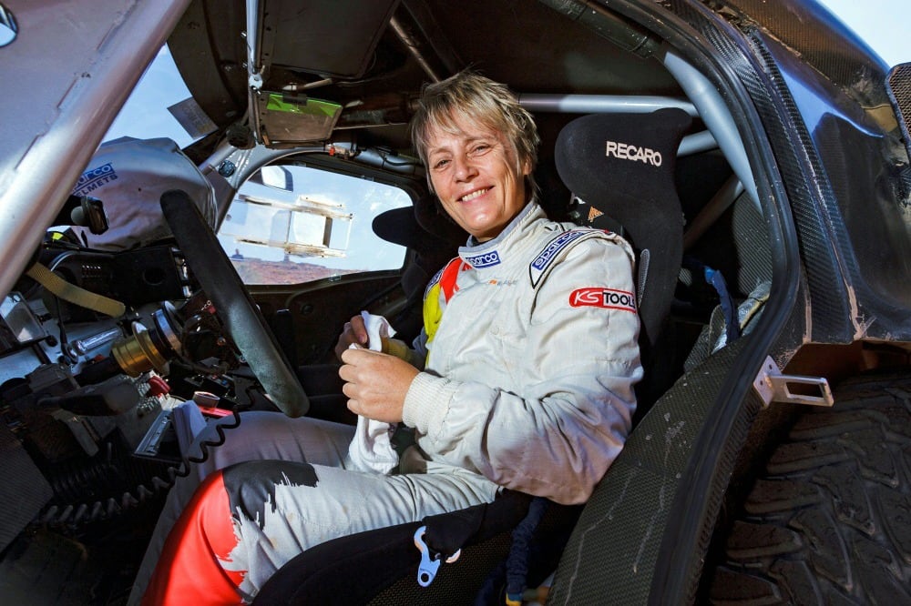 Kleinschmidt sonríe arriba de una auto de rally. 