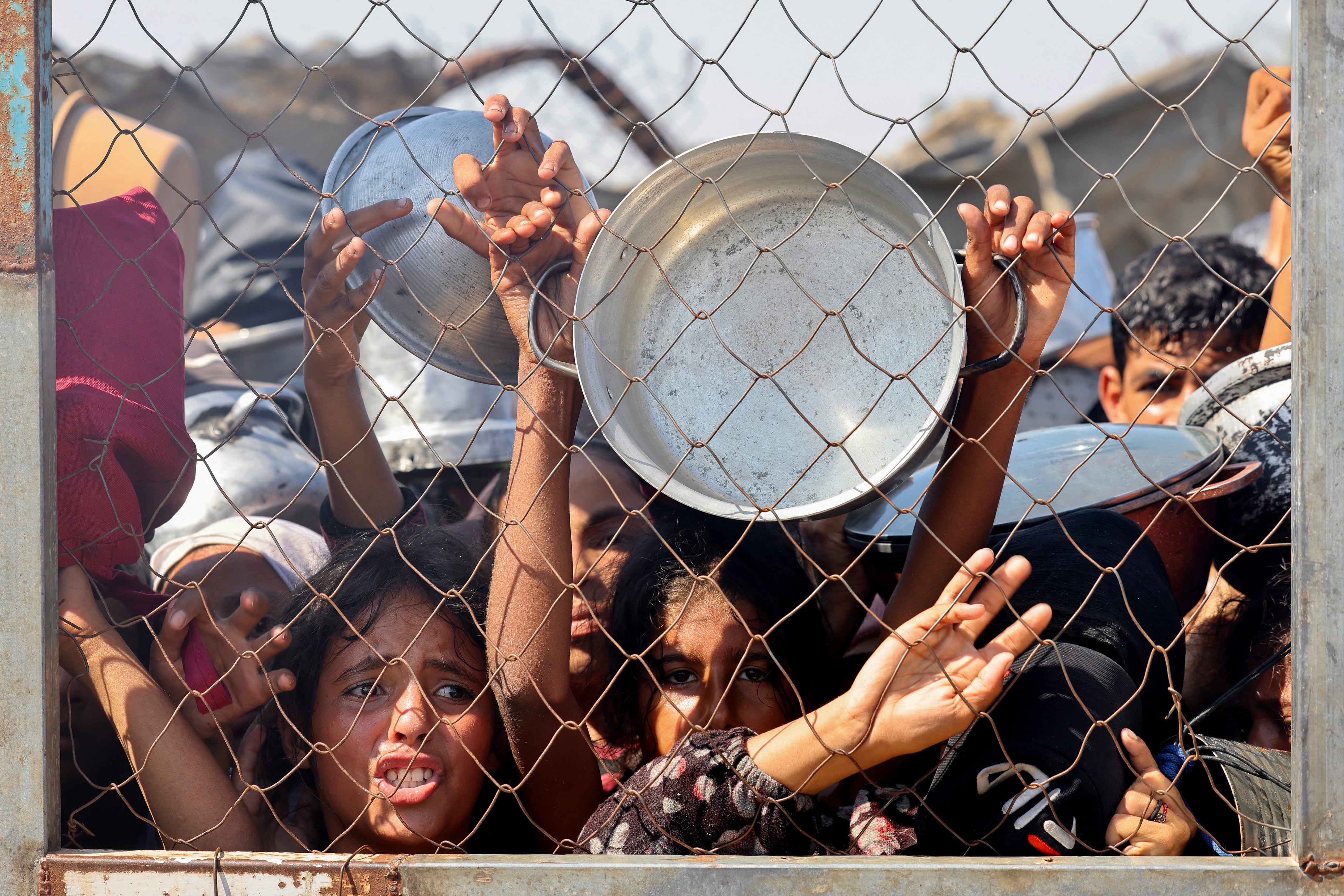 Palestinos, en su mayoría niños, se esfuerzan para recibir alimento en un comedor social de Mawasi, al sur de Gaza