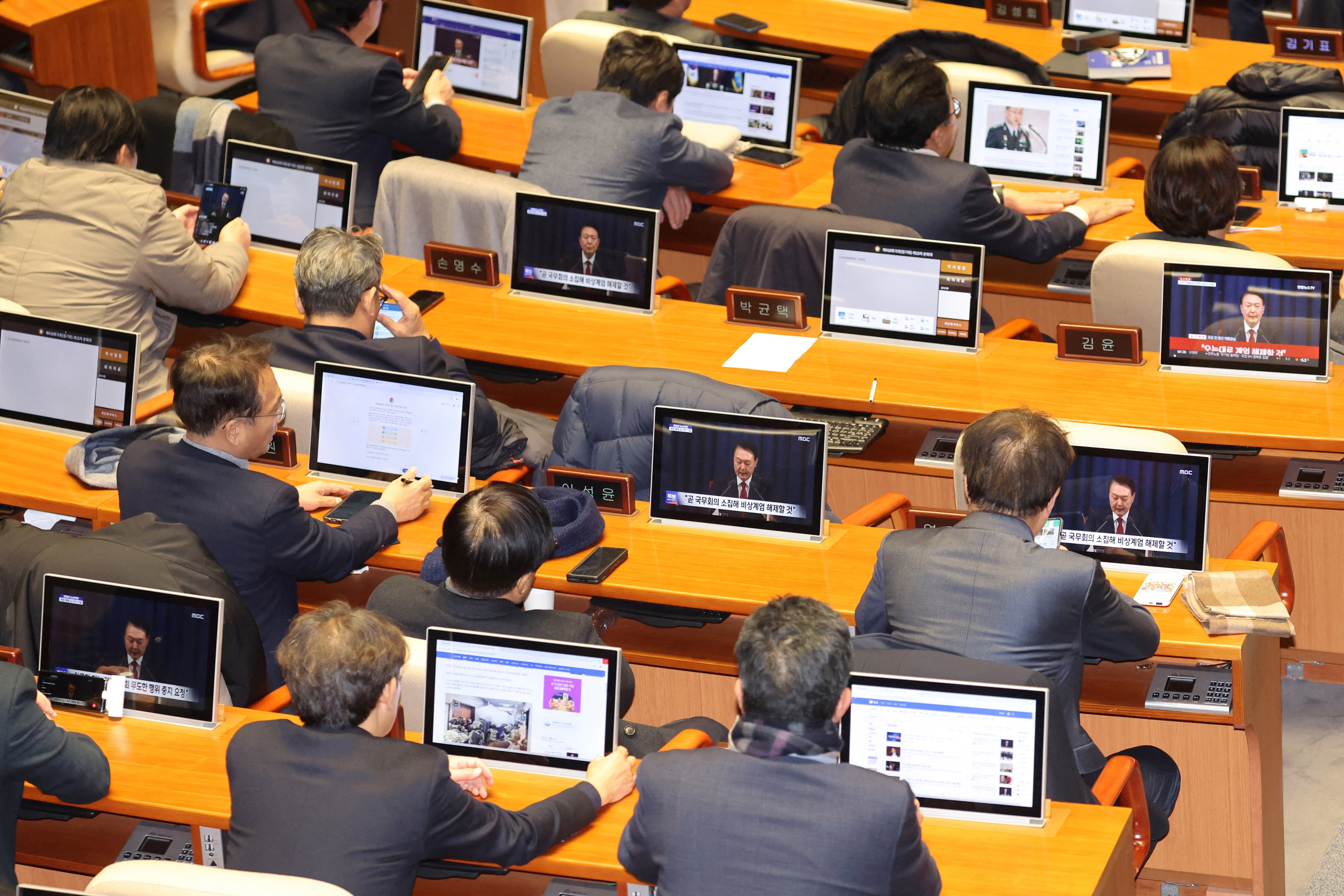 Congresits coreanos escuchan eldiscurso del preidente en el que levanta la ley marcial.