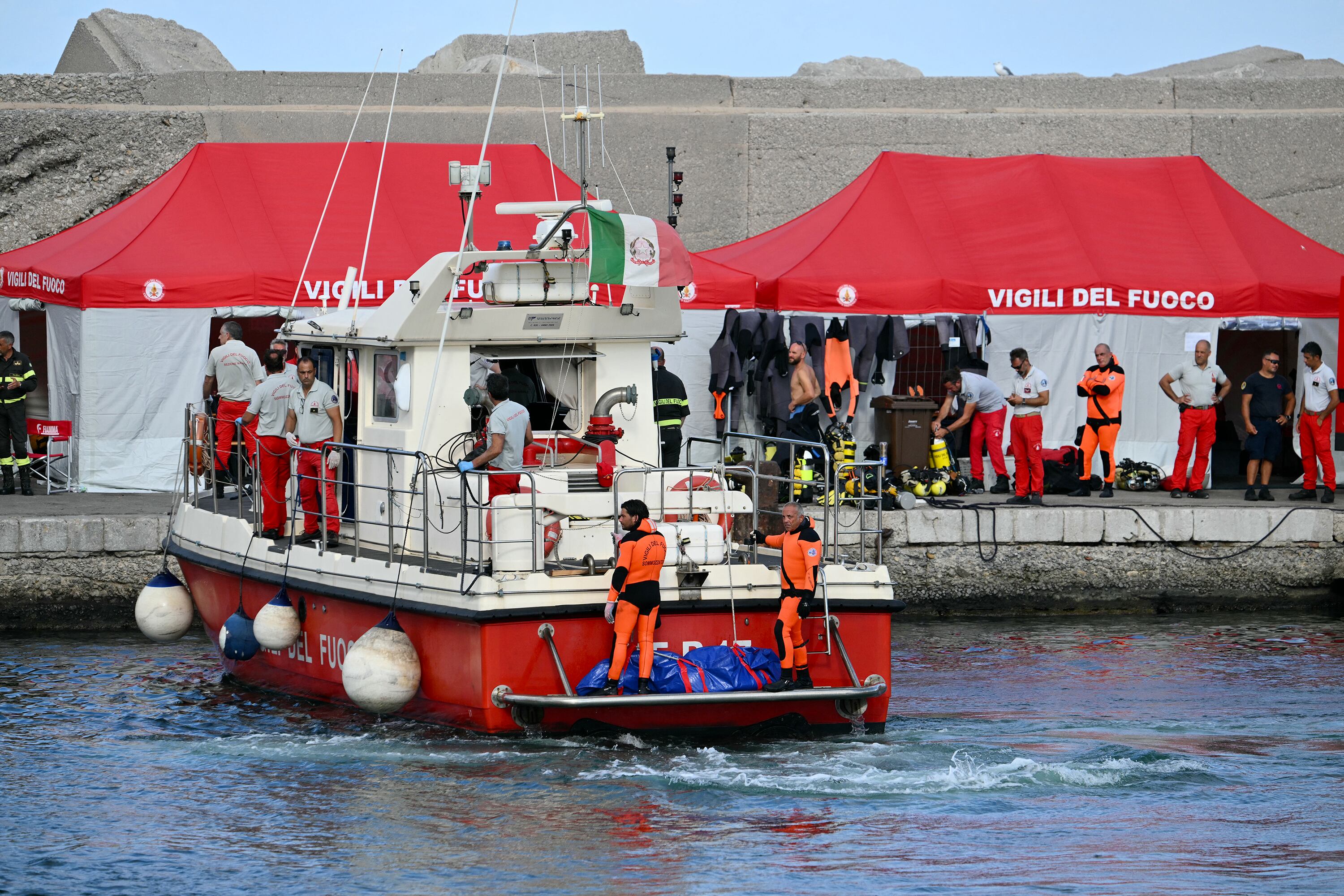 Buzos del Cuerpo de Bomberos italiano llegan al puerto de Porticello, cerca de Palermo, con un tercer cuerpo en la parte trasera del barco, dos días después de que se hundiera el yate de lujo Bayesian, de bandera británica. 
