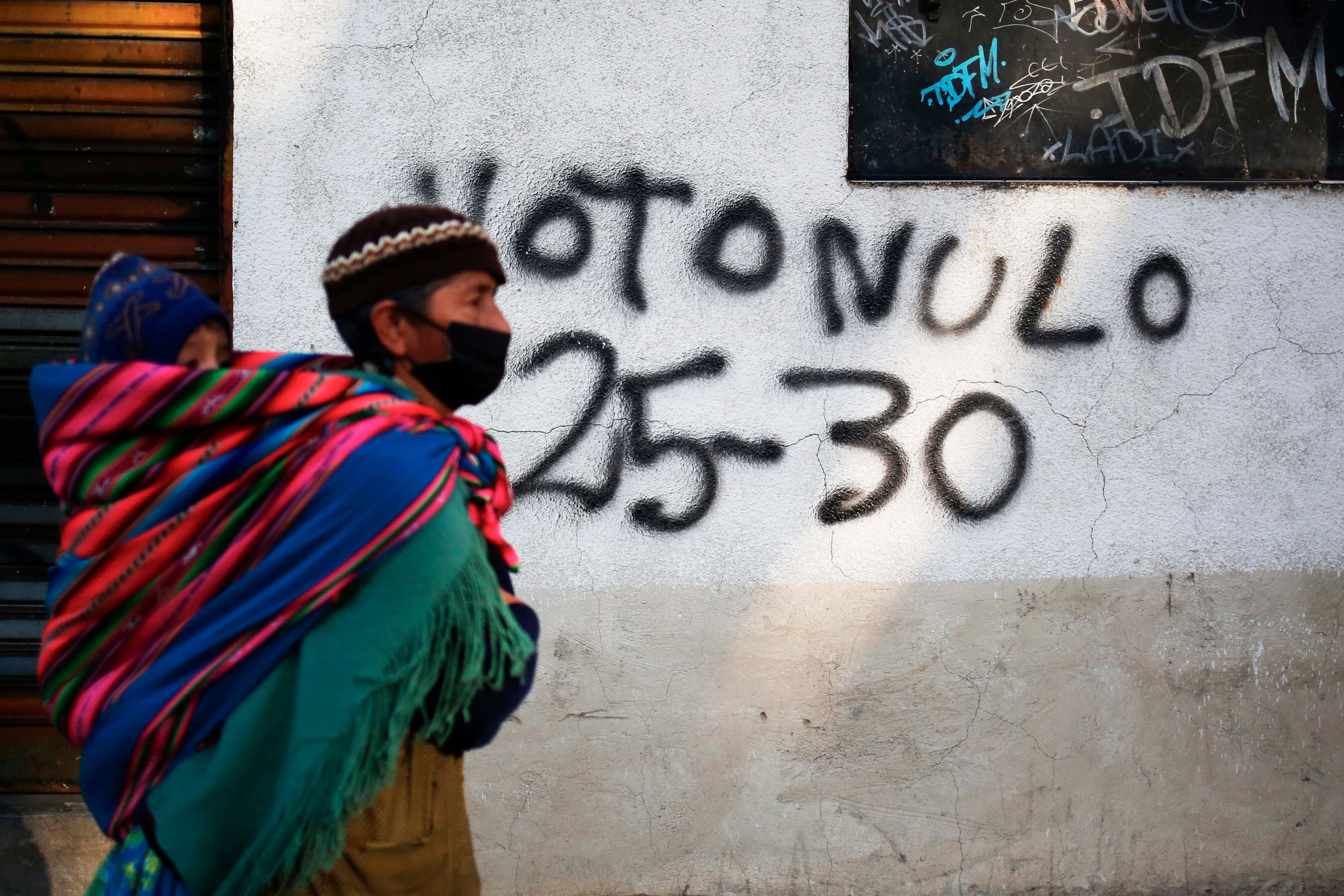 Una mujer aimara camina frente a una pintada electoral en La Paz.