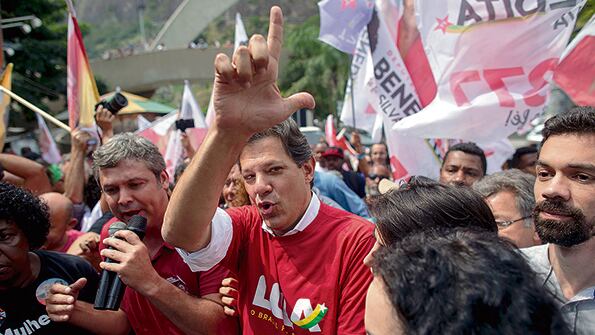 Rodeado por simpatizantes, Haddad hace la L de Lula con sus dedos durante su recorrida por Rocinha.