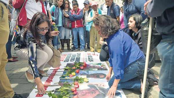 Amigos de las víctimas en Quito dejan flores en una bandera con las caras de los asesinados.