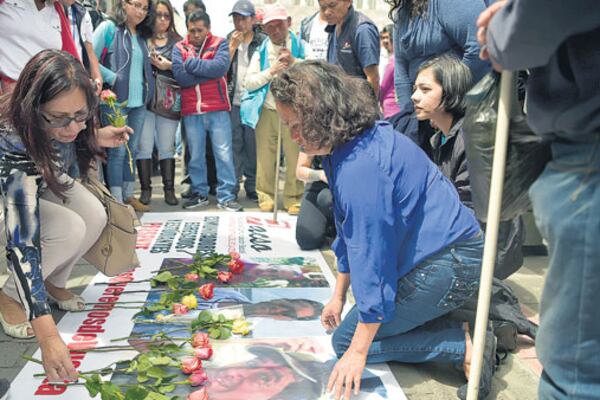 Amigos de las víctimas en Quito dejan flores en una bandera con las caras de los asesinados.