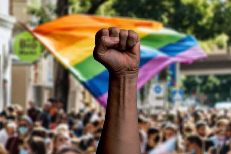 Puño en alto con una bandera LGBTQIA+ de fondo. Imagen: Freepik