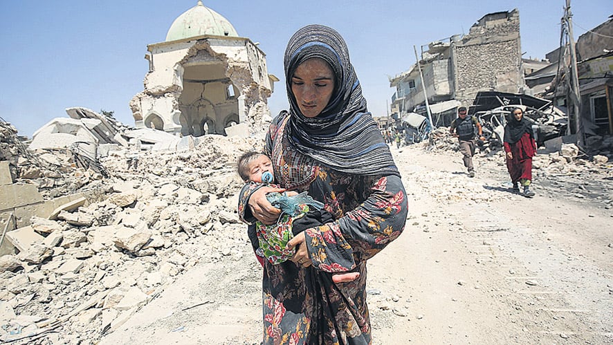 Una mujer camina con su bebé delante de las ruinas de mezquita de Al Nuri, en el oeste de Mosul.