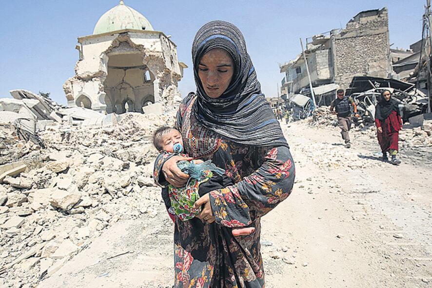 Una mujer camina con su bebé delante de las ruinas de mezquita de Al Nuri, en el oeste de Mosul.