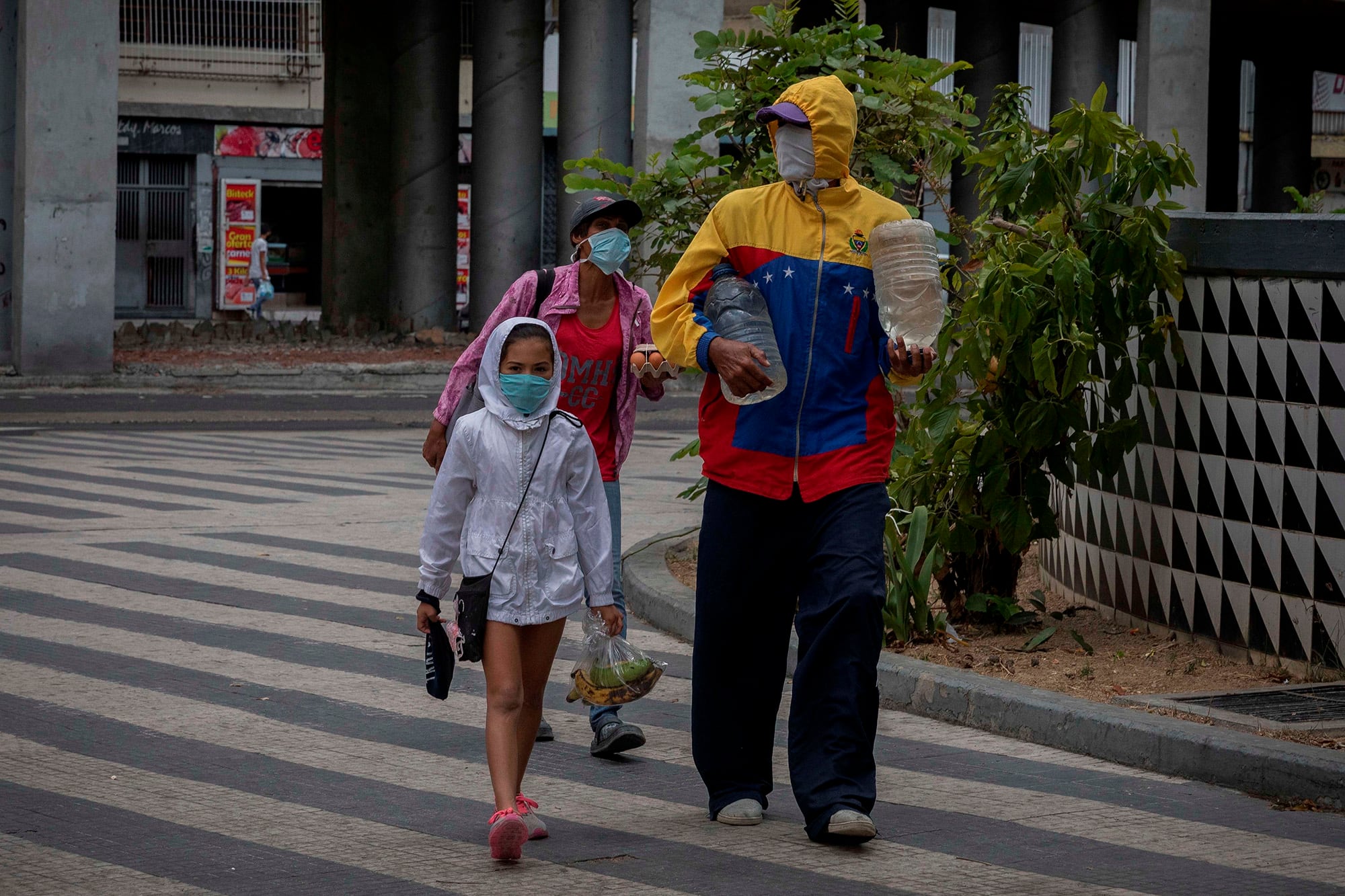 Una familia camina por las calles de Caracas cargando agua y fruta.