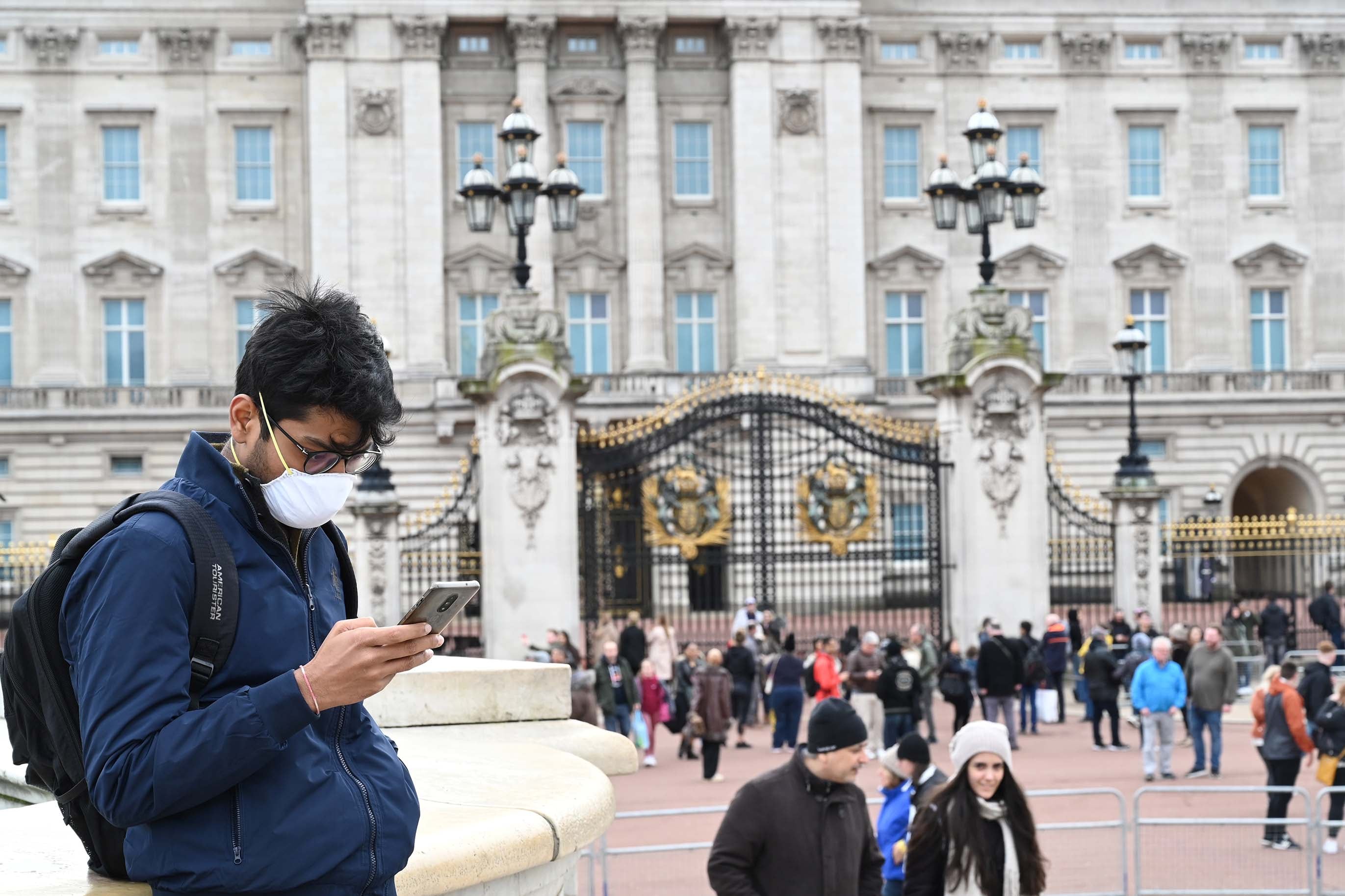 Un joven con barbijo mira su celular en la entrada a Buckingham Palace en Londres.