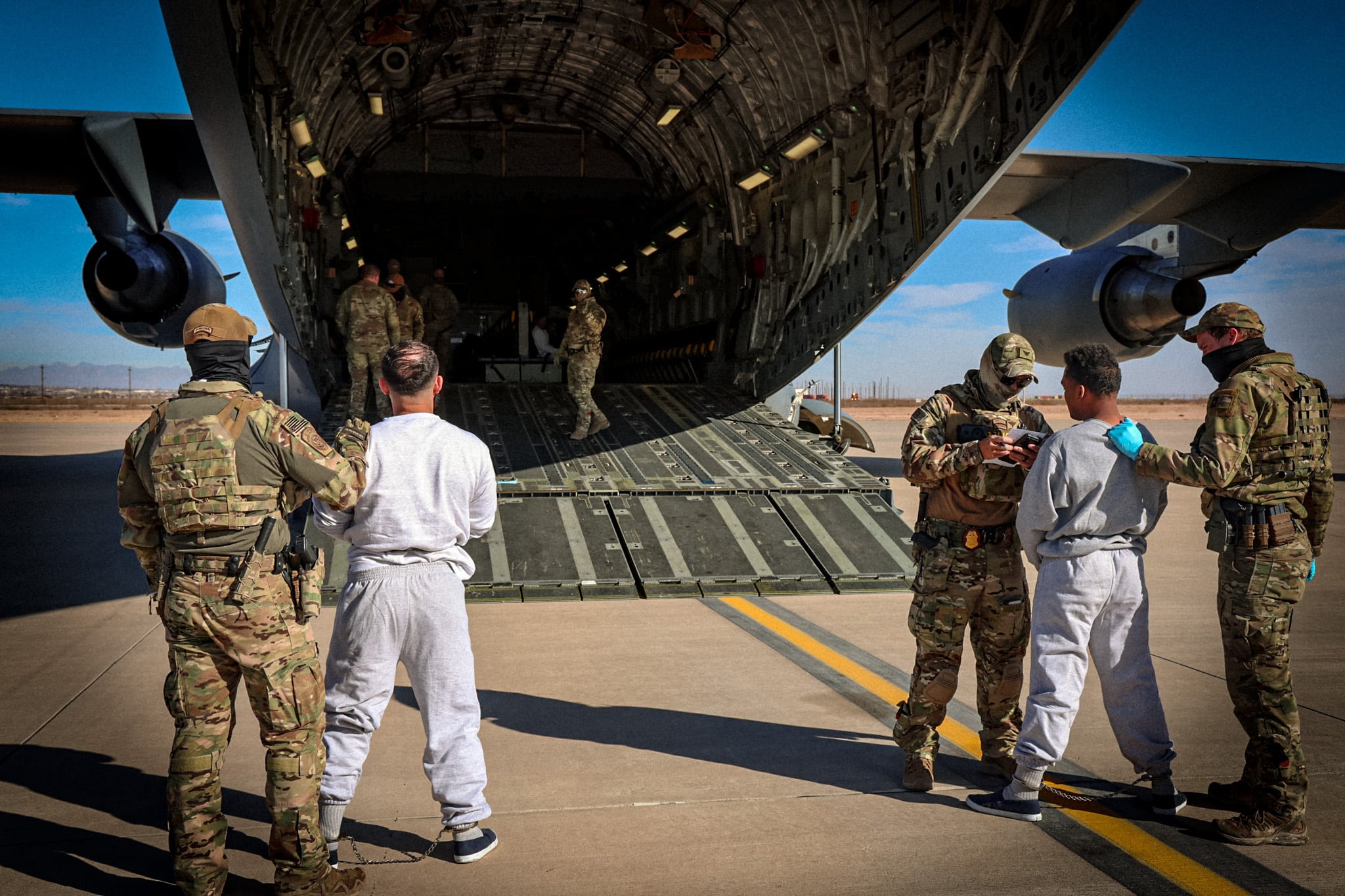 Inmigrantes detenidos parten encadenados con destino a la base de Guantánamo.