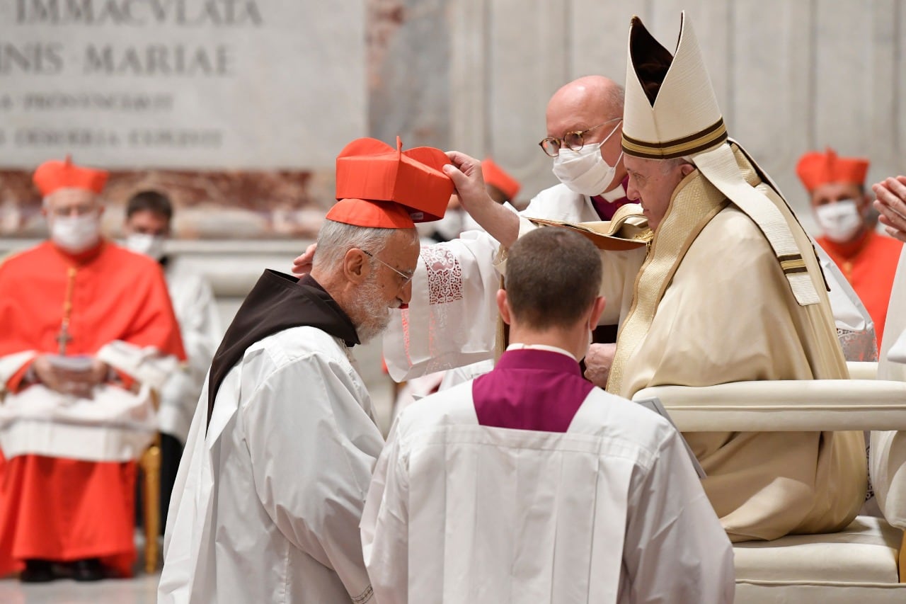El papa coloca el Capelo característico en la cabeza de uno de los nuevos cardenales.