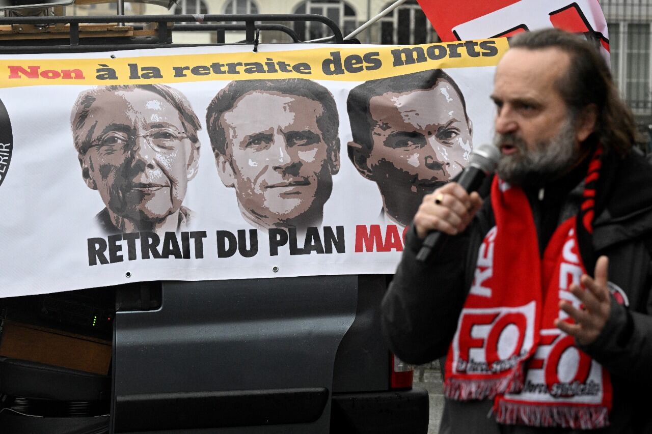 El líder sindical Fabrice Lerestif habla frente a un banner con las caras de la premier Borne, el presidente Macron y el ministro de Trabajo, Dussopt.  