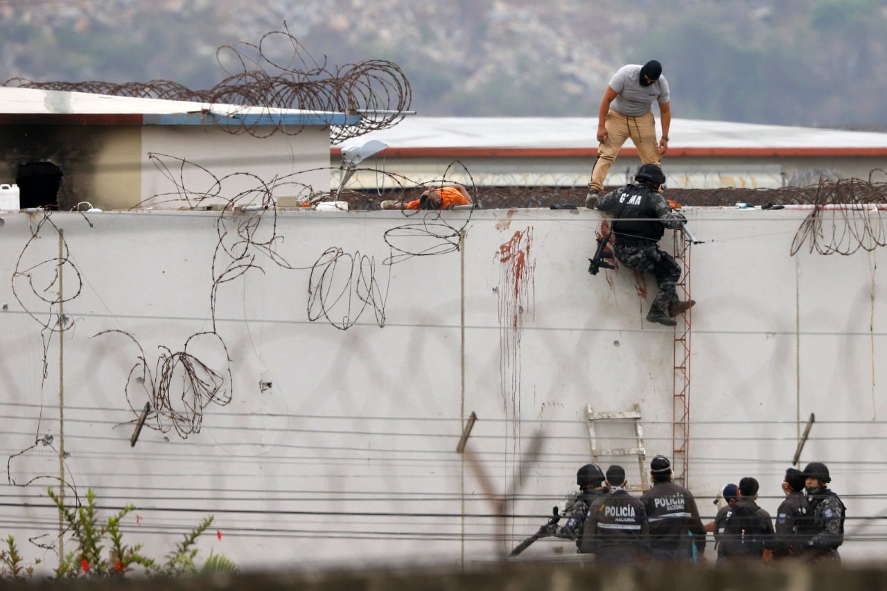 Policías ecuatorianos trepan un muro de la cárcel, donde yace el cuerpo de un recluso.