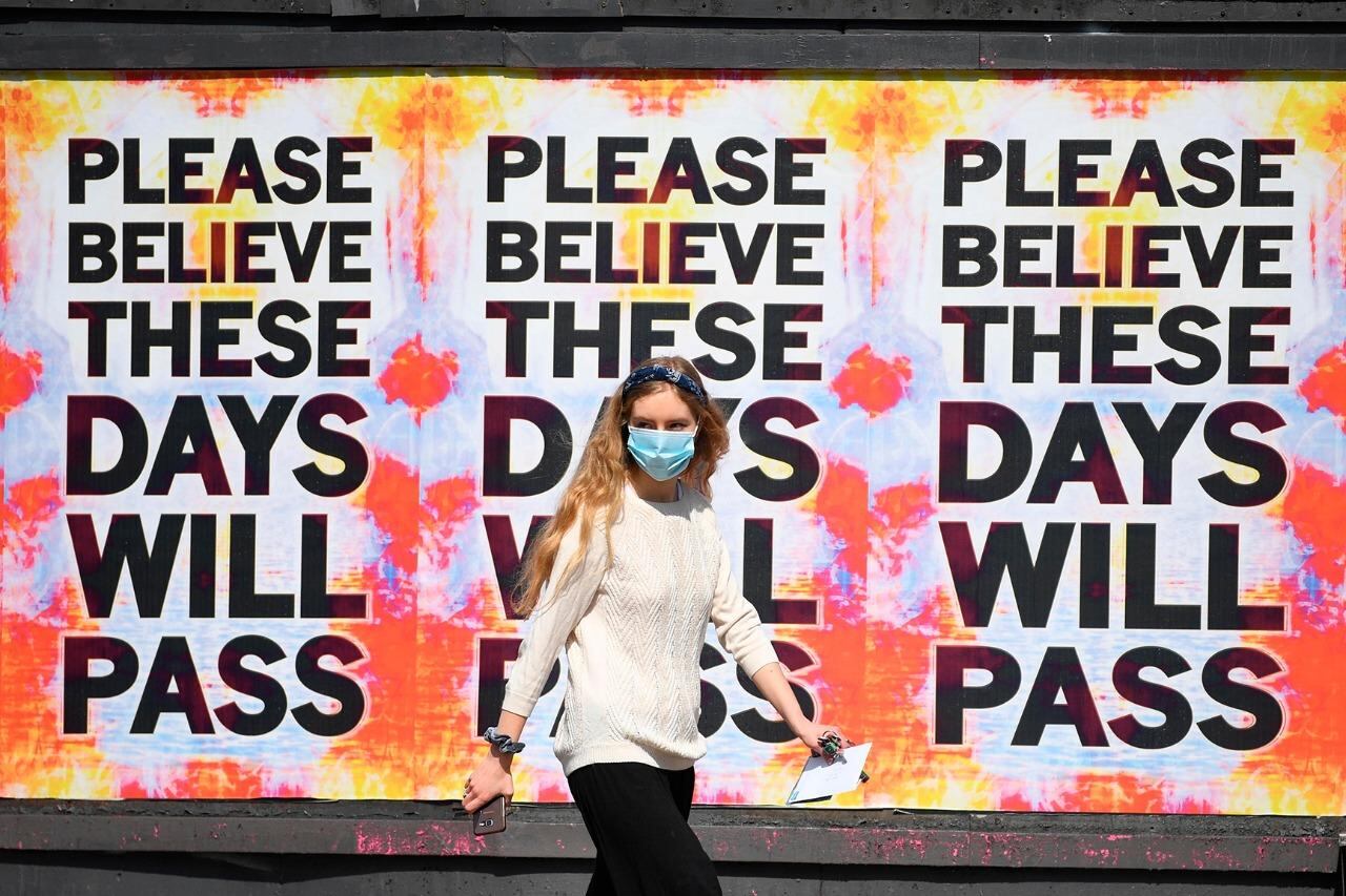 Una mujer con barbijo camina delante de carteles en Manchester.