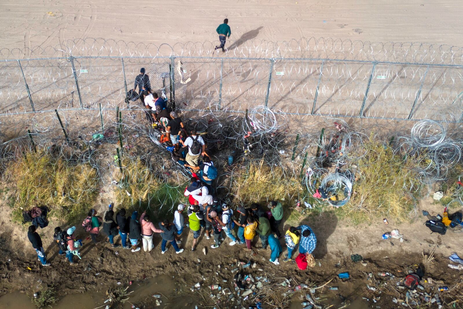 Inmigrantes cruzan la frontera por un agujero en el alambrado en El Paso, Texas.