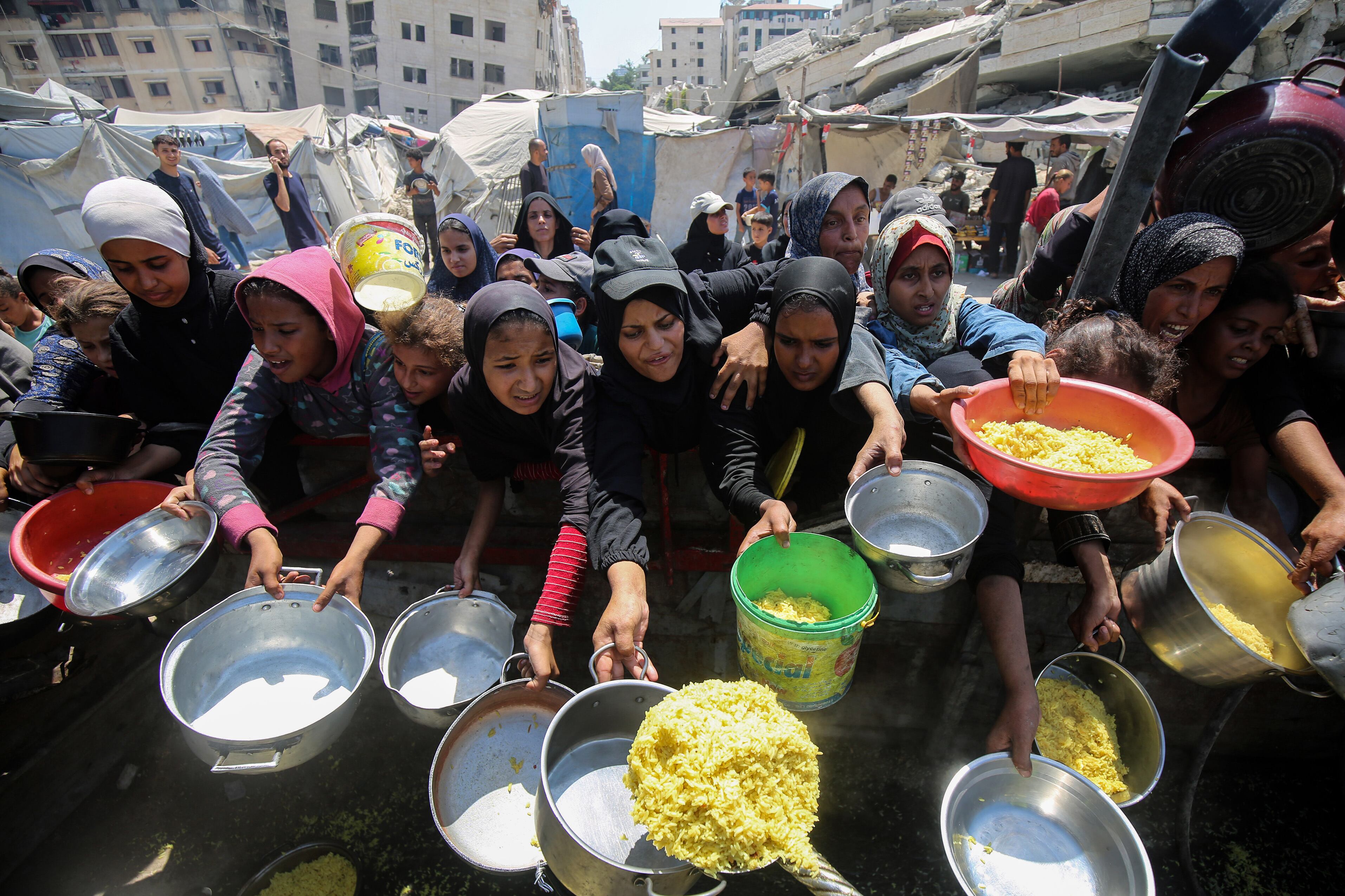 Mujeres palestinas intentan recibir alimentos en un campo para personas desplazadas, en el sudoeste de de Gaza