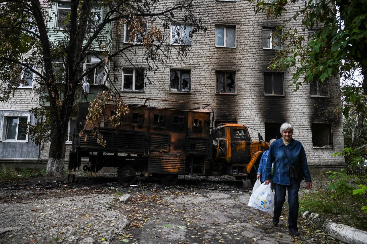 Dos mujeres caminan frente a una casa bombardeada en Balakliya, región de Kharkiv.