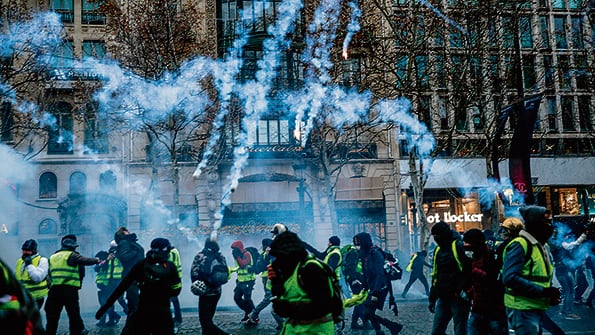 Chalecos amarillos resisten el gas lacrimógeno en los Champs-Elysées.