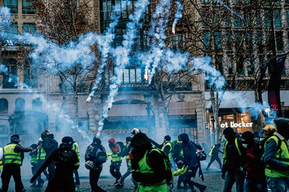Chalecos amarillos resisten el gas lacrimógeno en los Champs-Elysées.