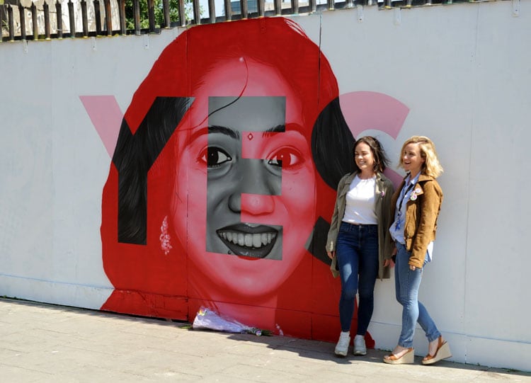 Do jóvenes posan frente a un mural por el Sí a la derecho a abortar.