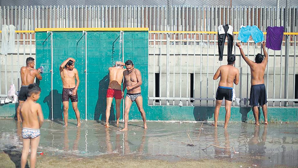Cientos de inmigrantes centroamericanos se bañan en duchas en un improvisado campamento.
