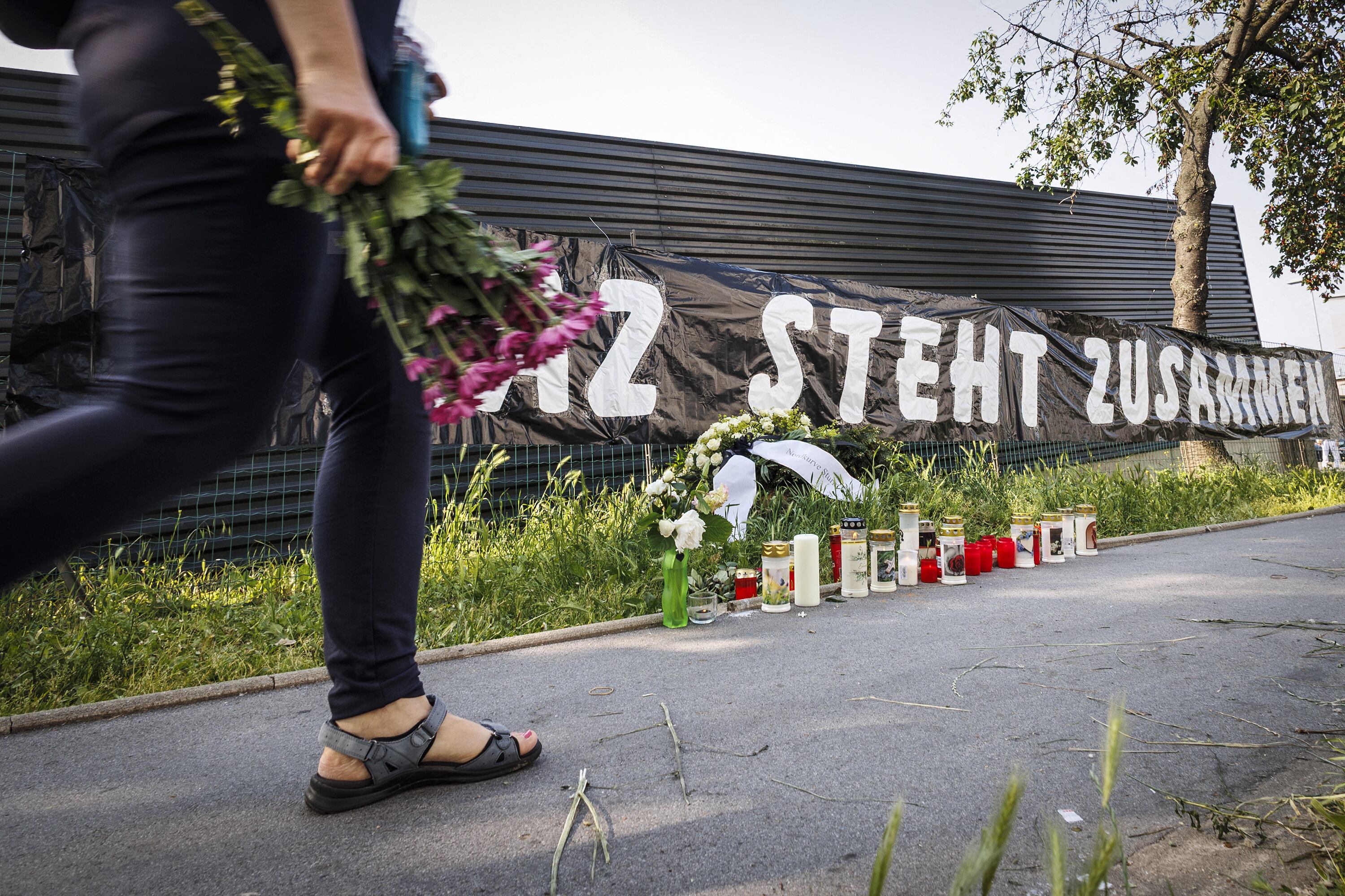 Una mujer con un ramo de flores camina junto a un cartel que dice "Graz se mantiene unida" en un memorial improvisado frente a la escuela.