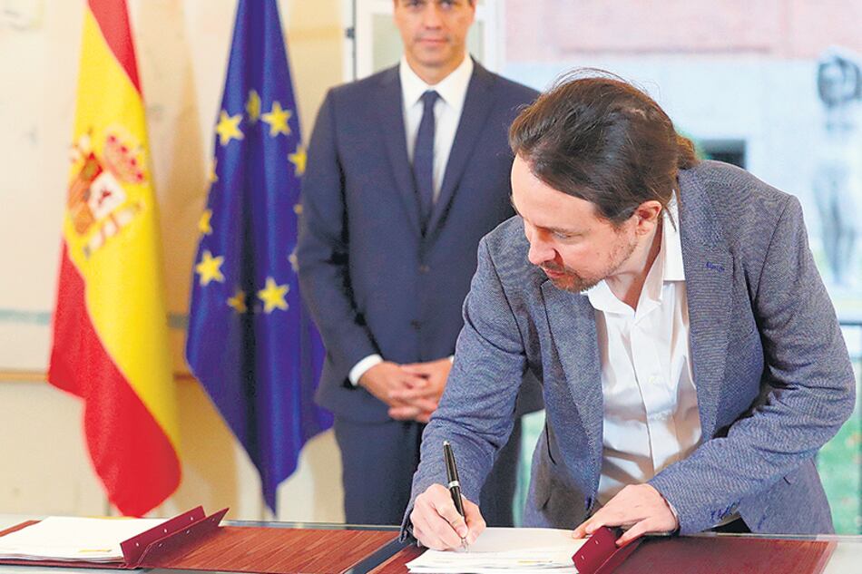 Iglesias firma el acuerdo bajo la atenta mirada de Sánchez ayer en Madrid.