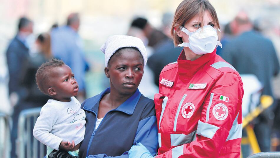 Una voluntaria de la Cruz Roja italiana asiste a una refugiada con su niño en Salerno.