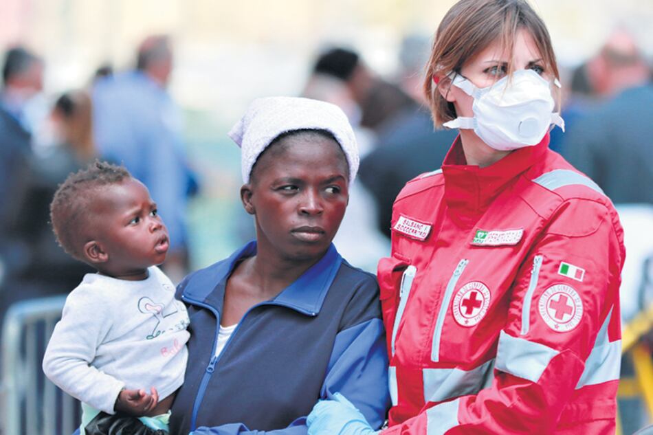 Una voluntaria de la Cruz Roja italiana asiste a una refugiada con su niño en Salerno.