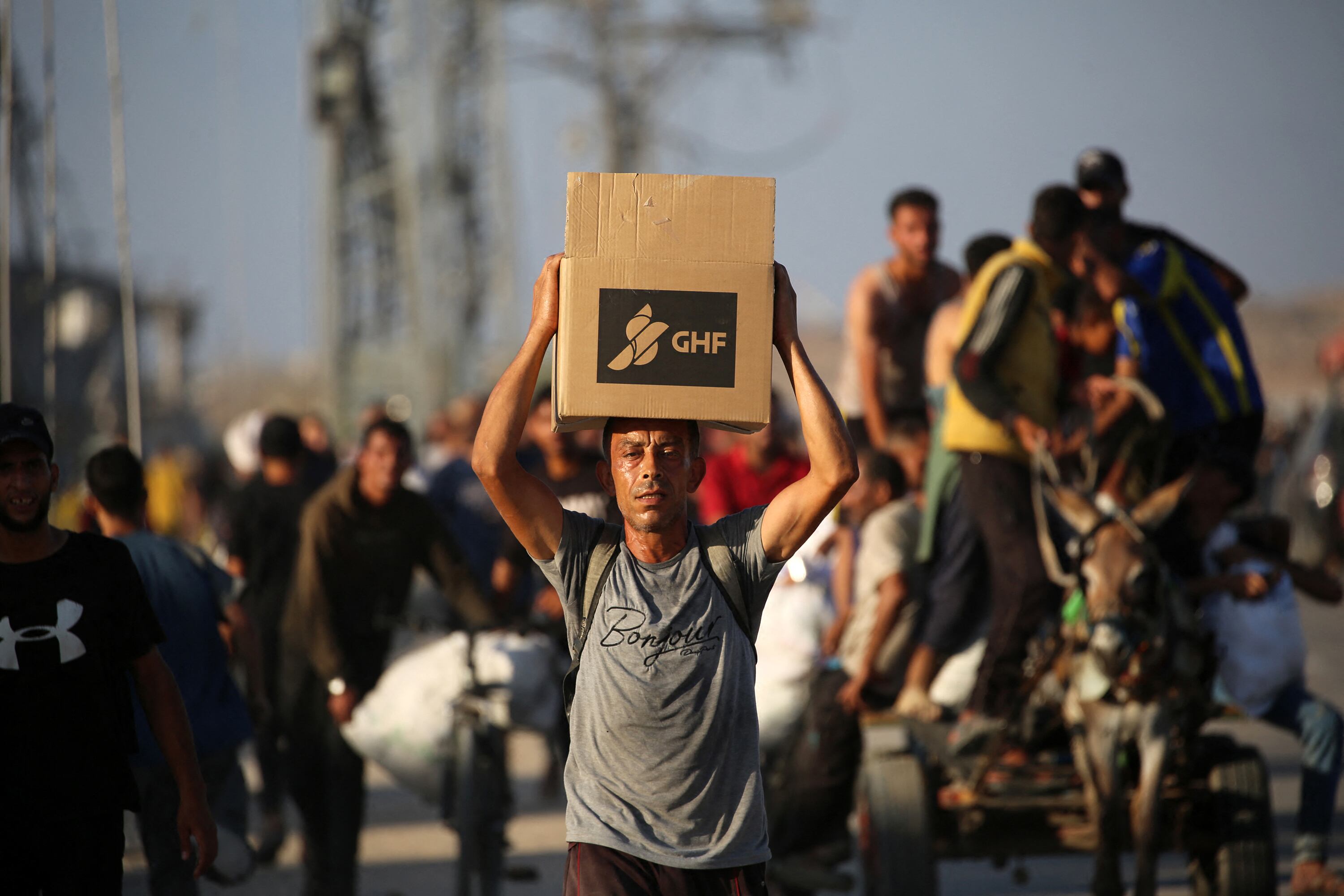 Un palestino camina cargando una caja de alimentos por la ruta de Salaheddin, cerca del campo de refugiados de Nuseirat