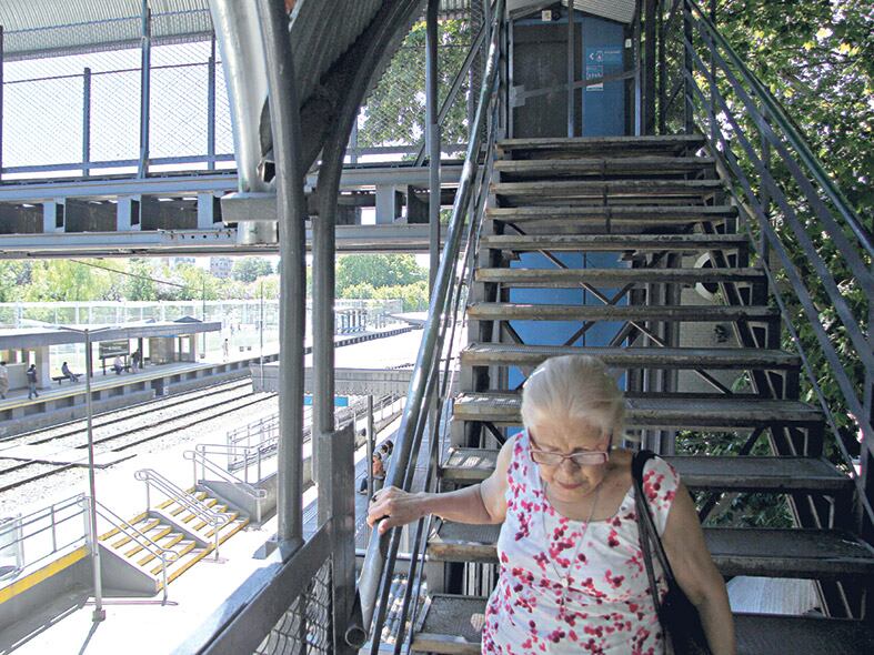 Una mujer se esfuerza para bajar la escalera del puente y llegar al anden a tomar el tren.