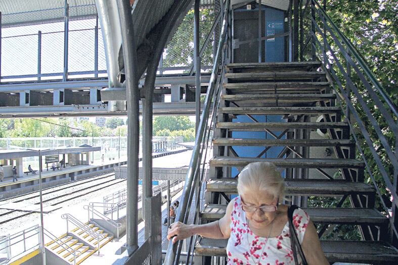 Una mujer se esfuerza para bajar la escalera del puente y llegar al anden a tomar el tren.