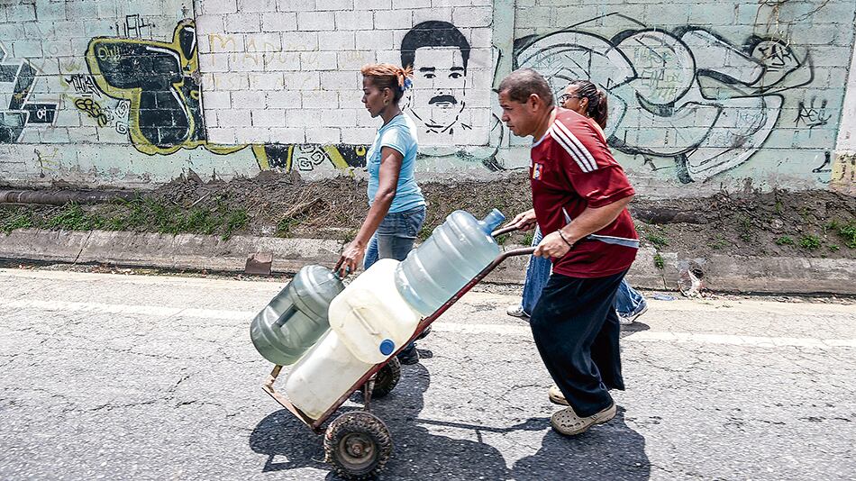 Un hombre empuja un carretilla con bidones cargados en un canal de aguas servidas en Caracas.