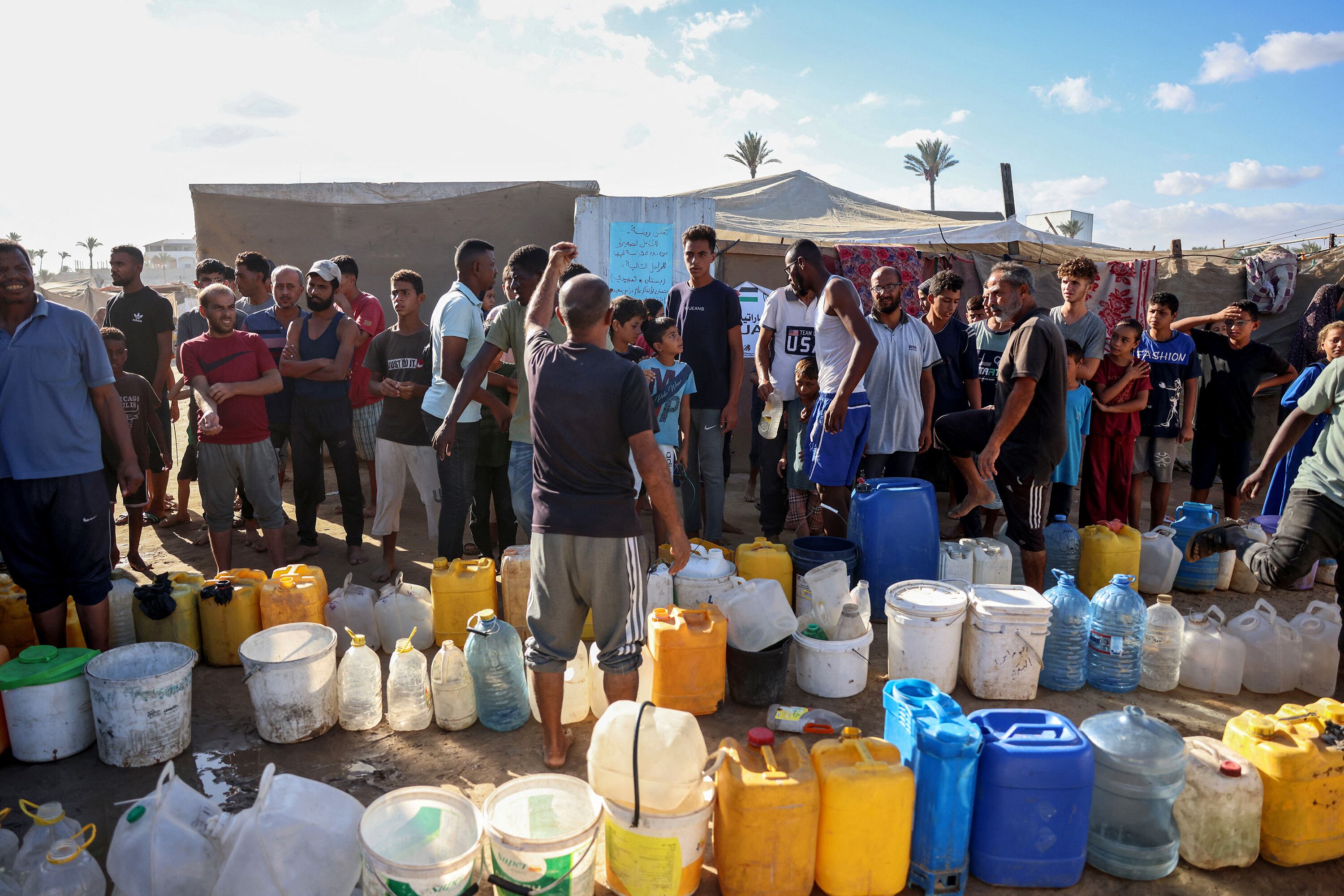 Palestinos desplazados forman fila para cargar agua en Gaza.