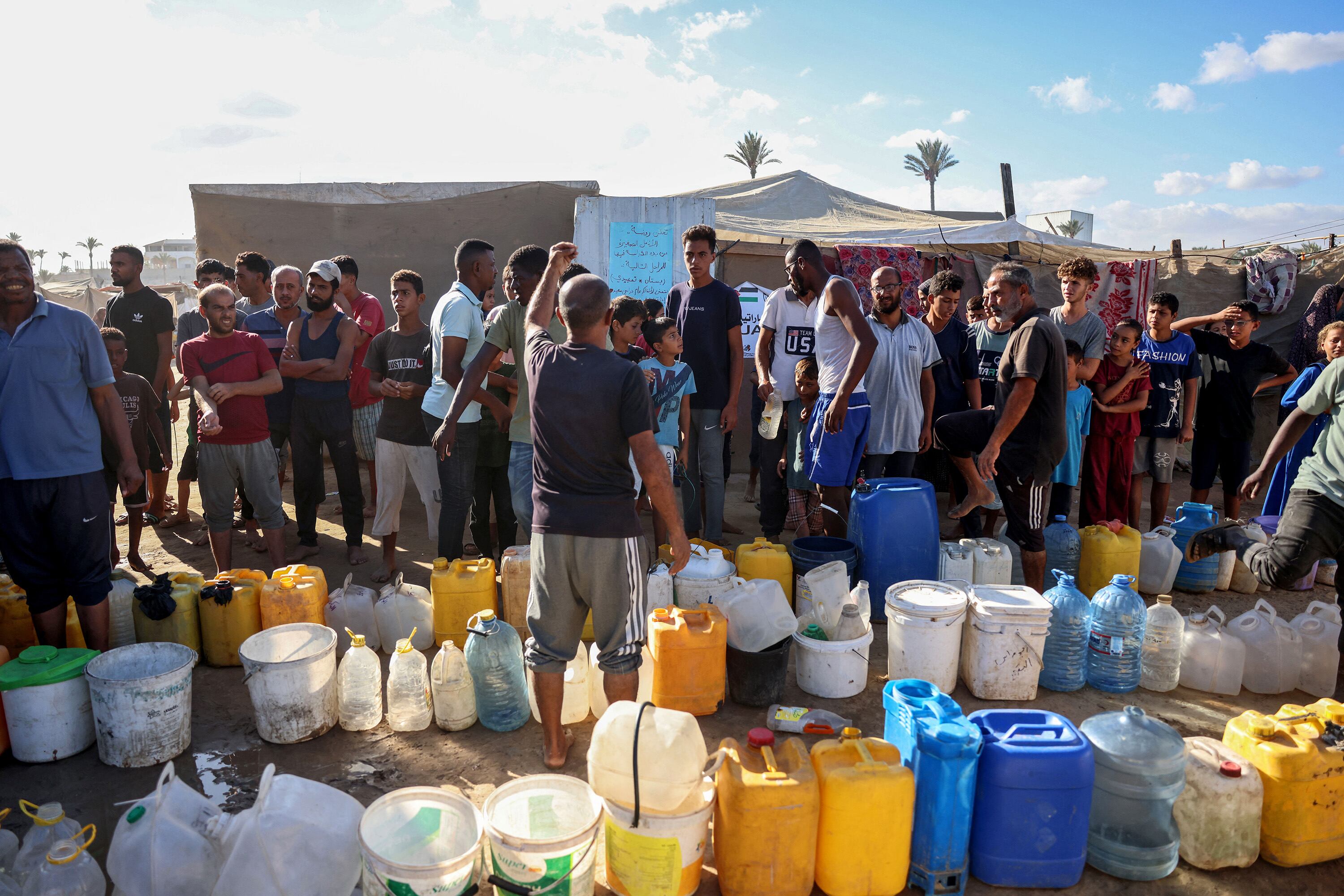 Palestinos desplazados forman fila para cargar agua en Gaza.