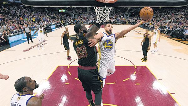Curry lanza ante la oposición de James, mientras Durant espera el desenlace de la jugada.