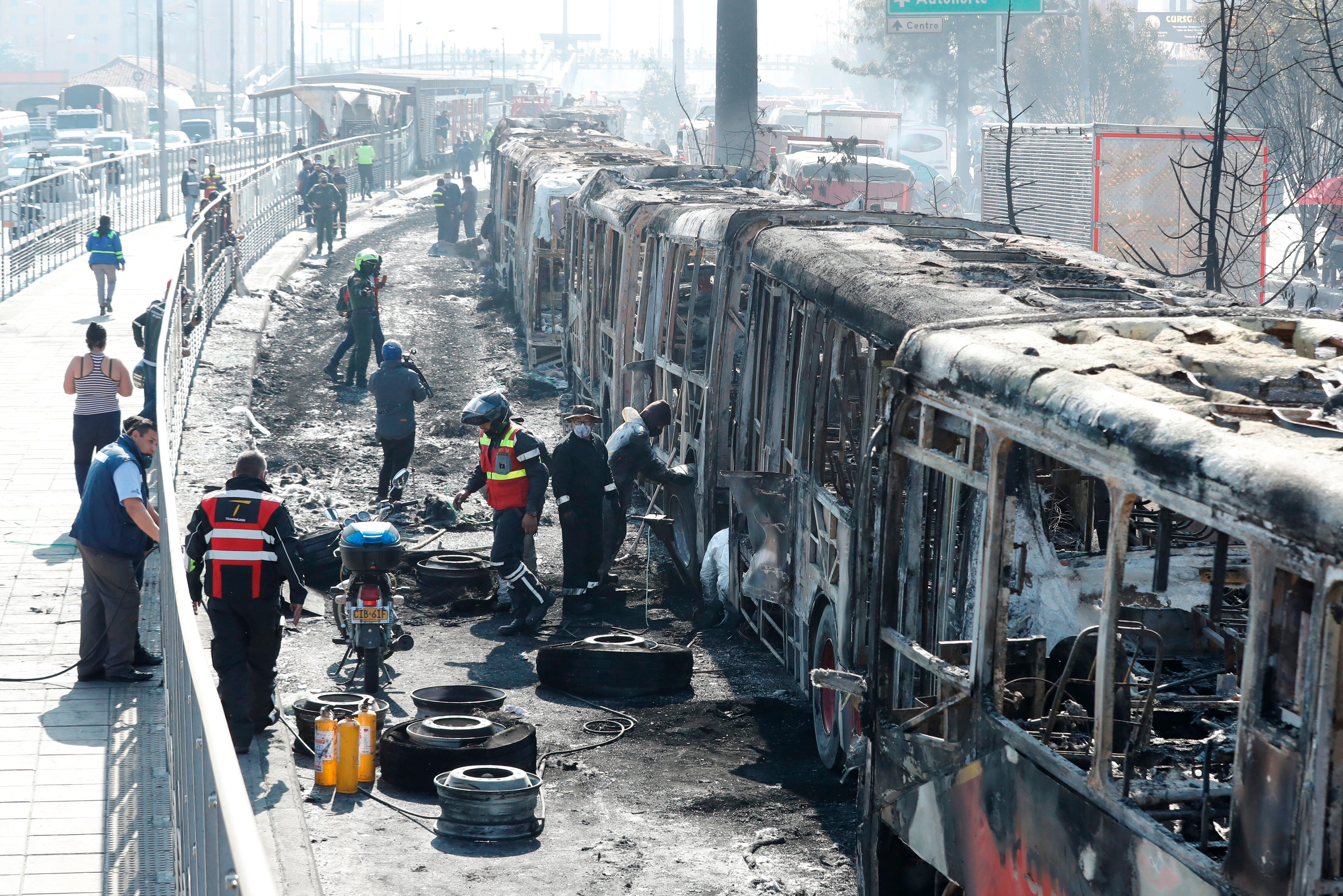 Funcionarios y peritos trabajan con los restos de buses de TransMilenio incinerados durante las protestas. 