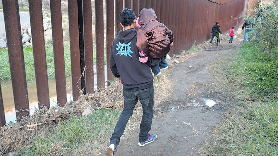 Un migrante con un niño en brazos camina en la frontera ente San Diego y Tijuana.