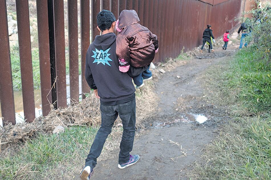 Un migrante con un niño en brazos camina en la frontera ente San Diego y Tijuana.