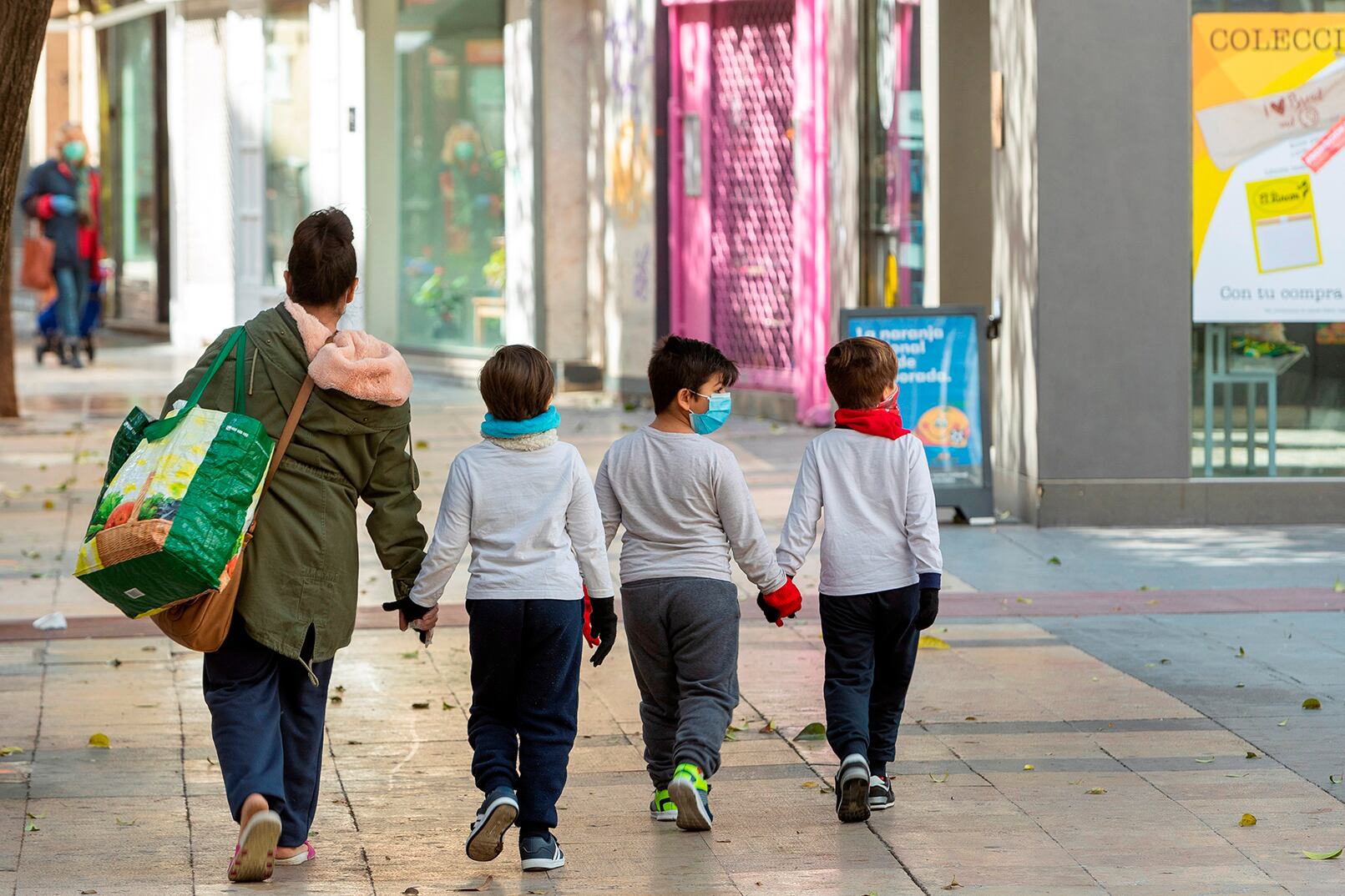 Una mujer y tres niños con guantes y barbijos caminan de la mano en Zargoza.