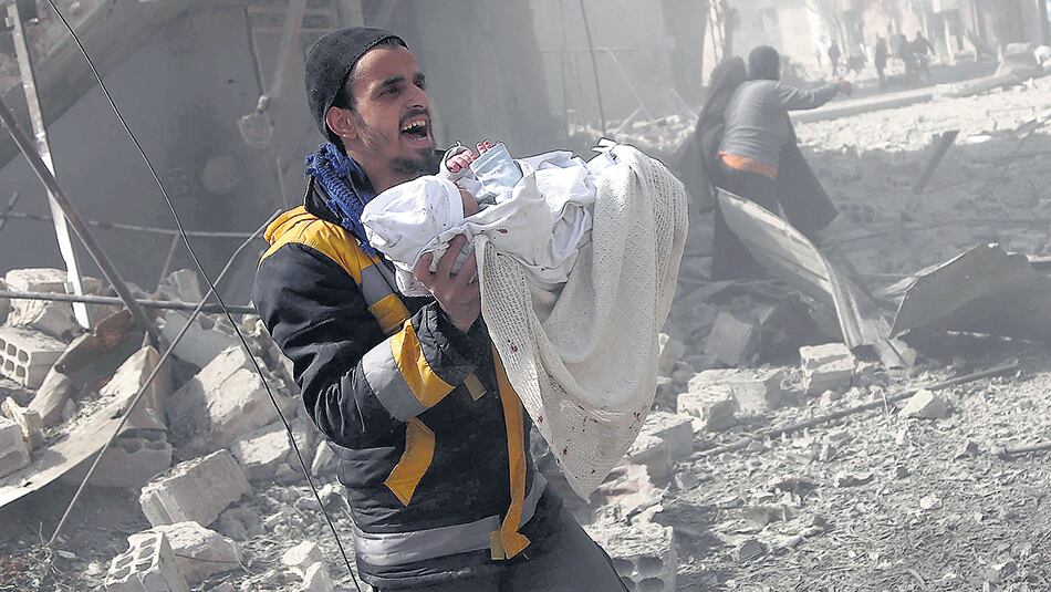 Un hombre cargaba a un niño rescatado de un bombardeo ayer en Hamouria, Guta Oriental.