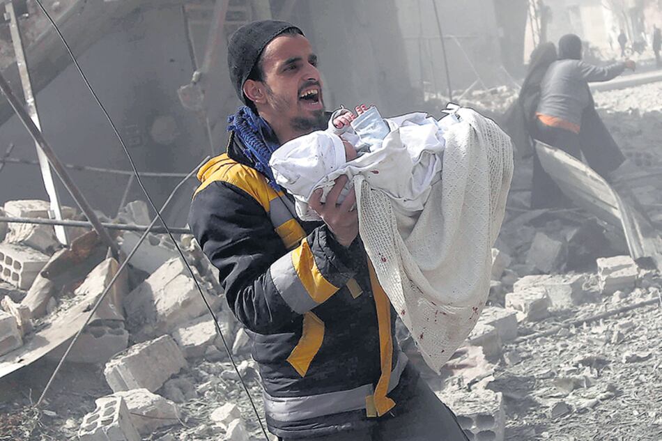 Un hombre cargaba a un niño rescatado de un bombardeo ayer en Hamouria, Guta Oriental.