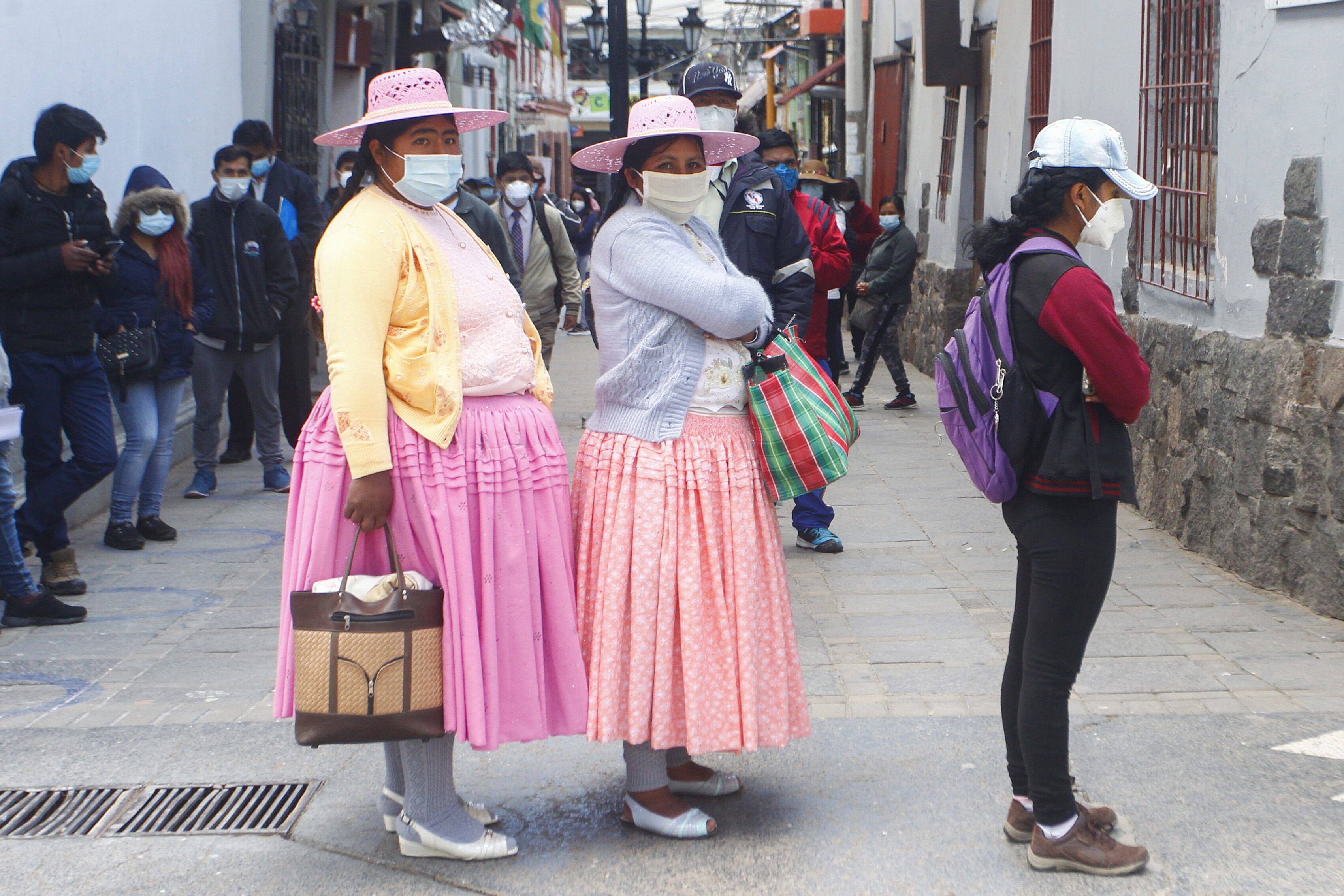 Mujeres con vestidos tradicionales y barbijo hacen fila para entrar a un banco en Puno. 2. Controles sanitarios en el aeropuerto de Lima. (EFE)
