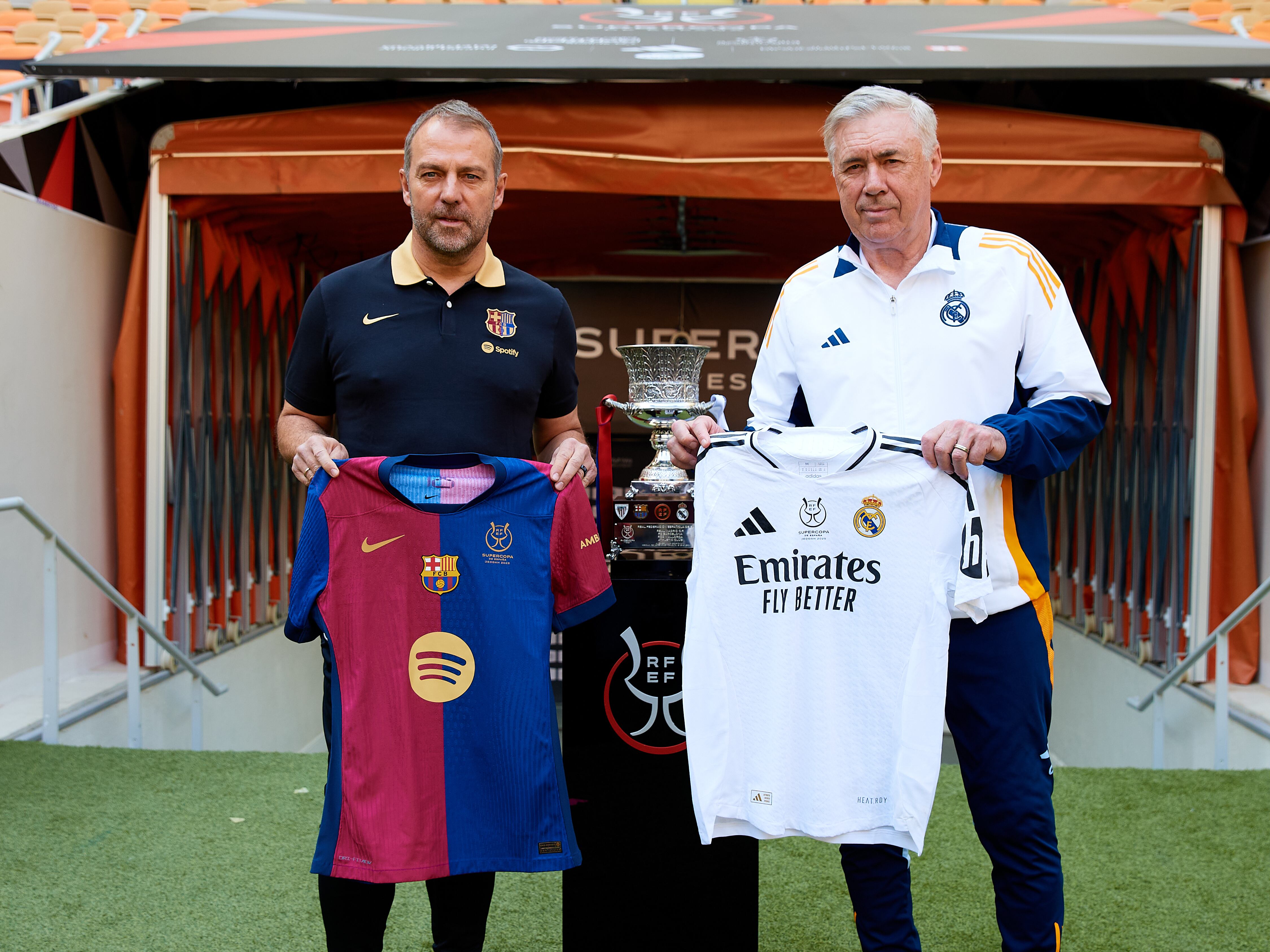 Hansi Flick y Carlo Ancelotti posan con casacas de sus equipos junto al trofeo